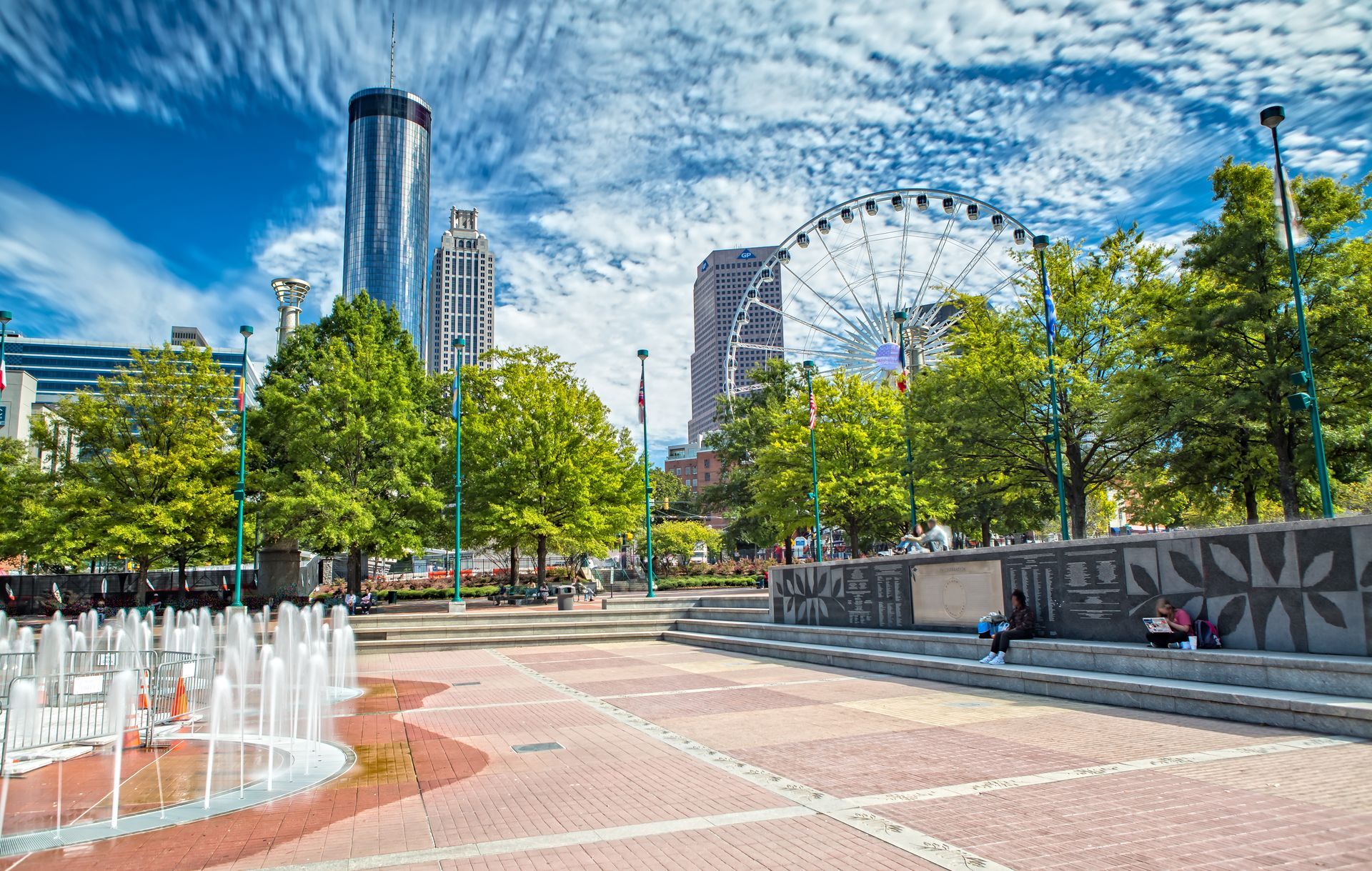 A fountain in a park with a ferris wheel in the background.
