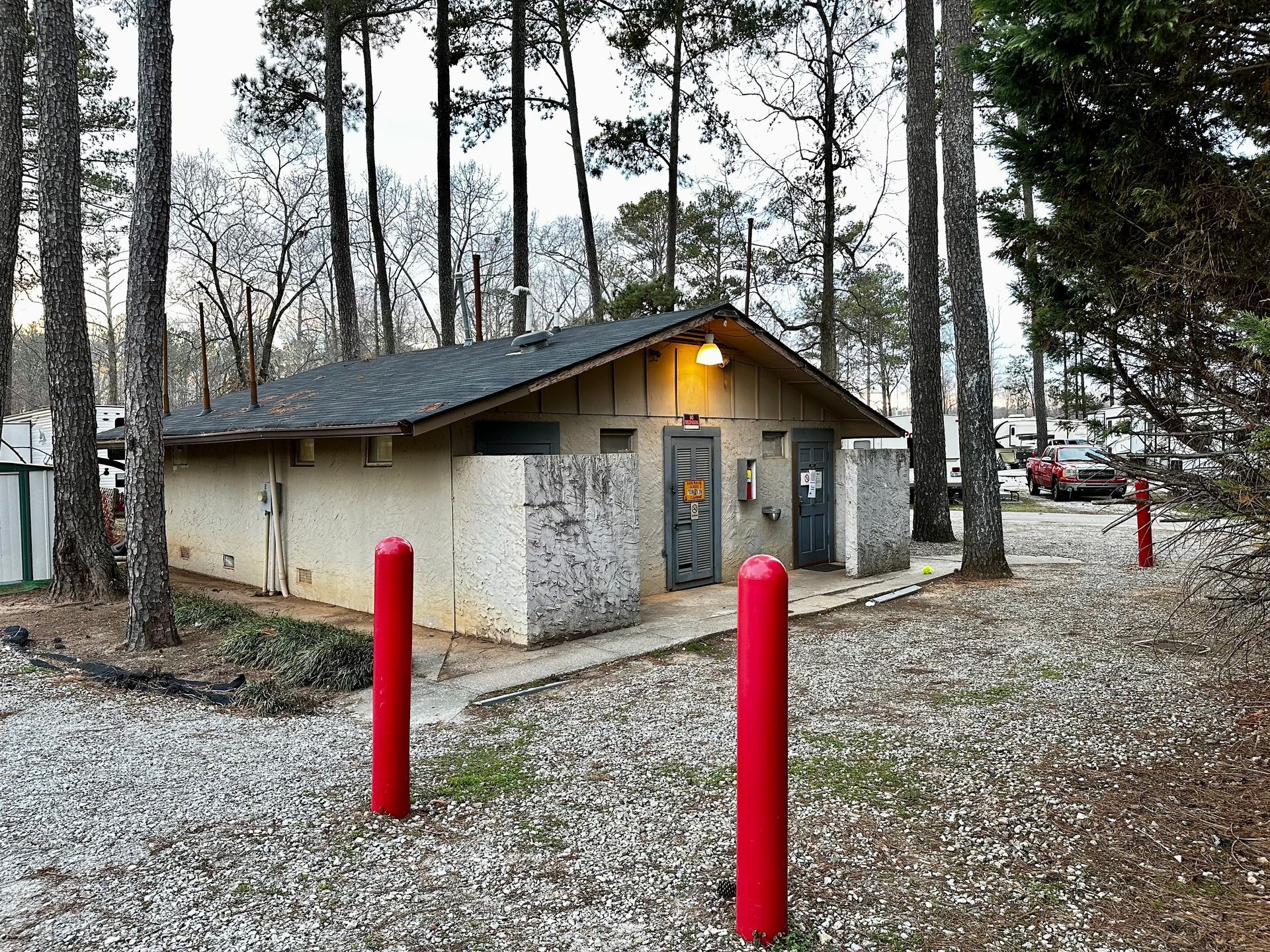 A small building in the middle of a forest with red poles in front of it.