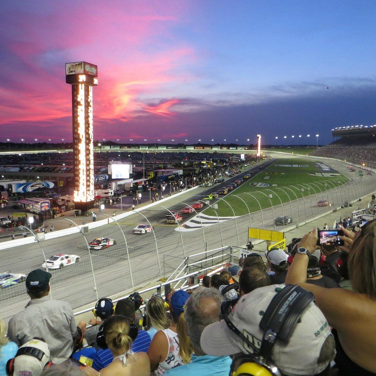 A crowd of people watching a race with a coca cola tower in the background