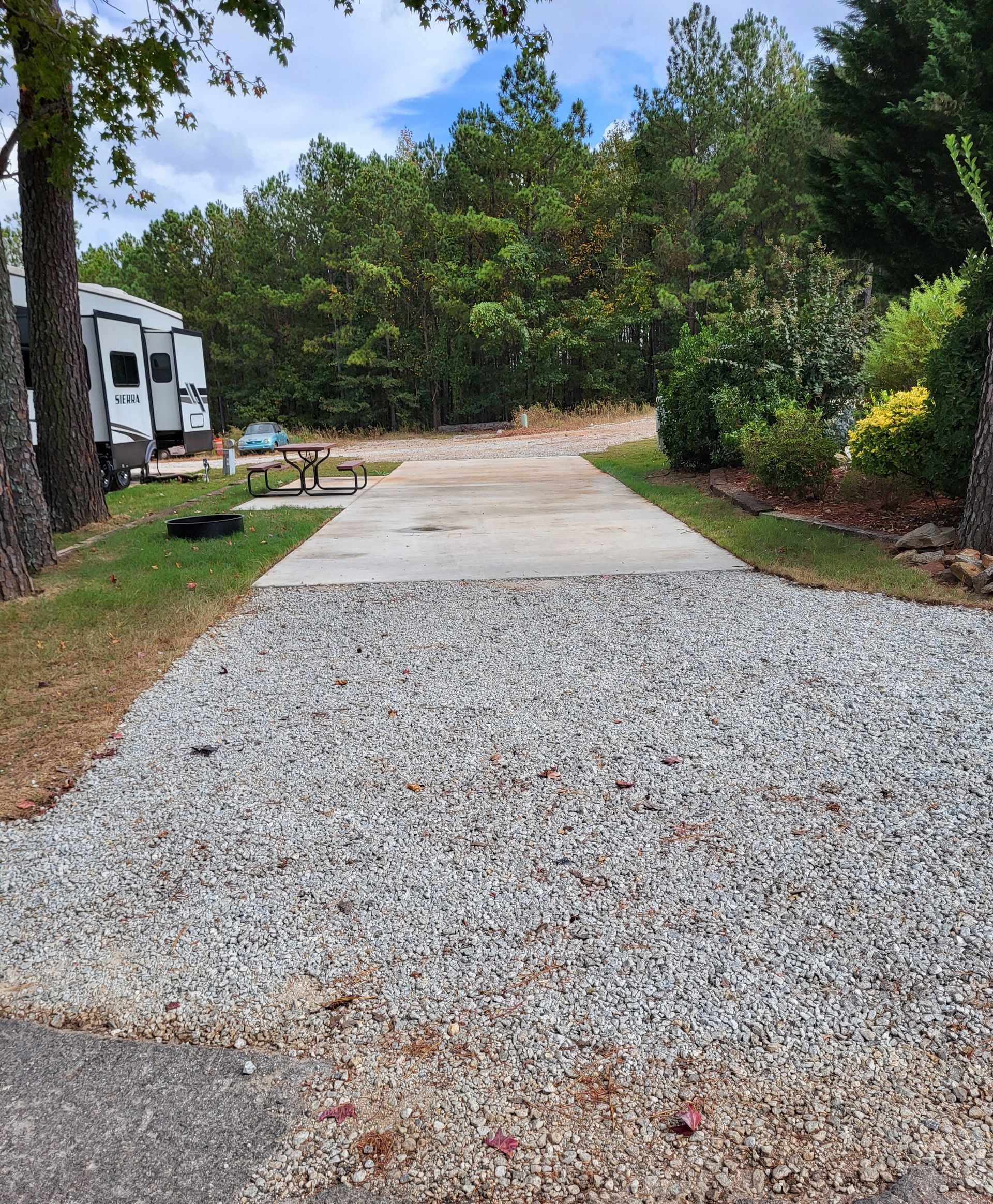 A gravel driveway leading to a rv parked in the woods.