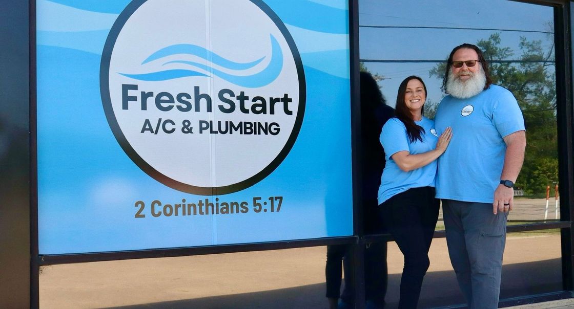 A man and a woman are standing in front of a fresh start a / c and plumbing sign.