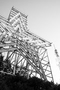 Black-and-white view of a large metal electrical transmission tower against the sky.