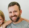 A man with a beard is smiling while holding a little girl.