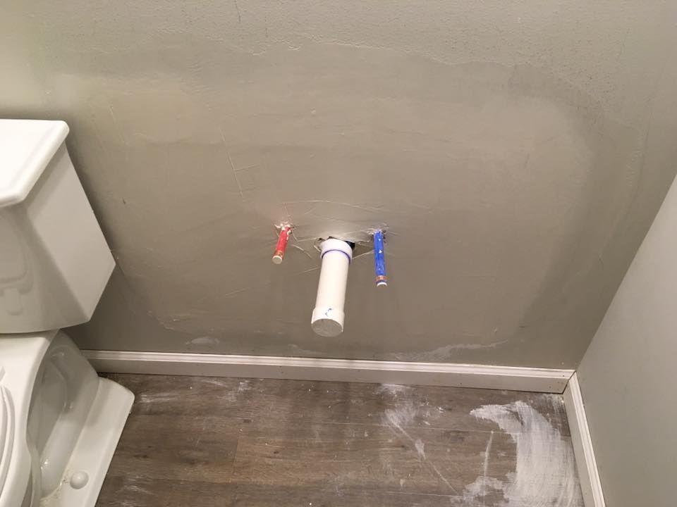 A bathroom with a toilet , sink and pipes on the wall.