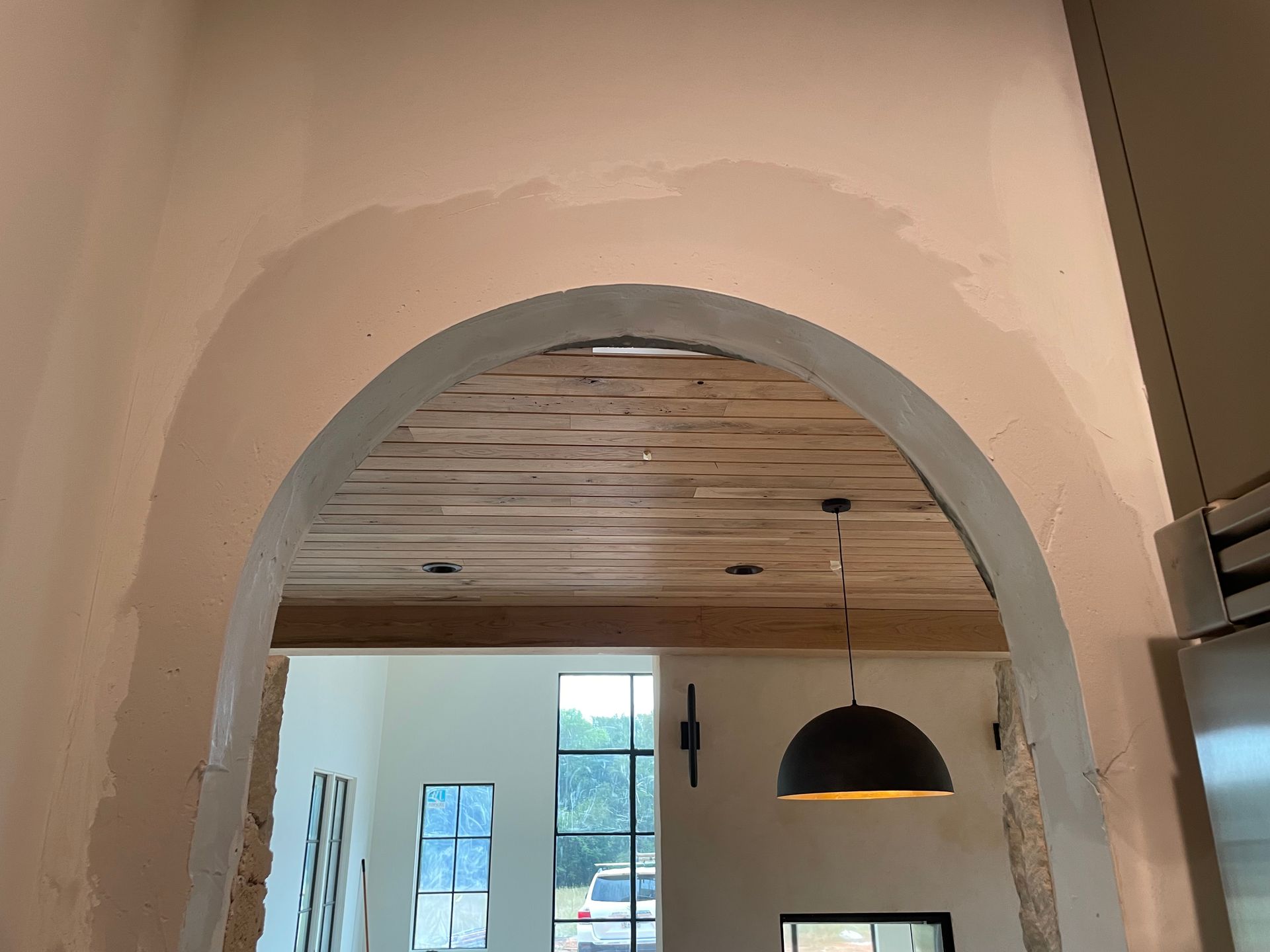 A room with a drywall arch and wooden ceiling and a hanging light.