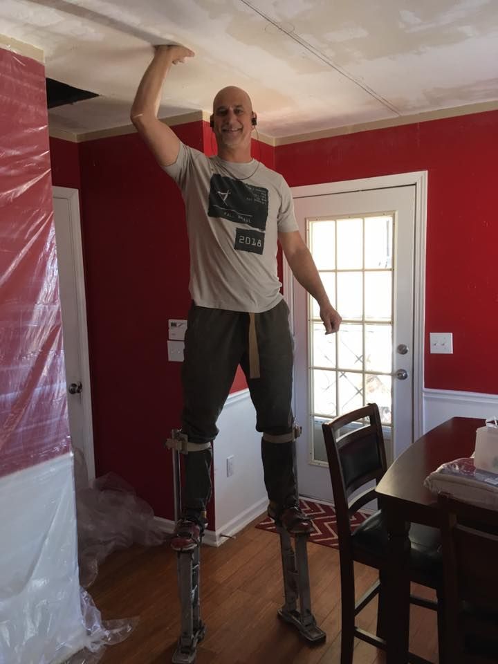 A man is standing on stilts in a room with red walls.