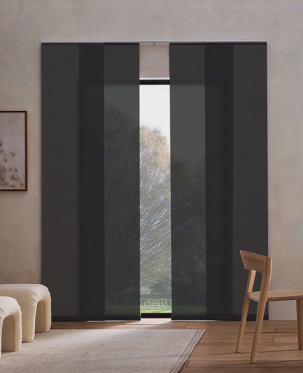 A living room with a large window and black panel blinds.