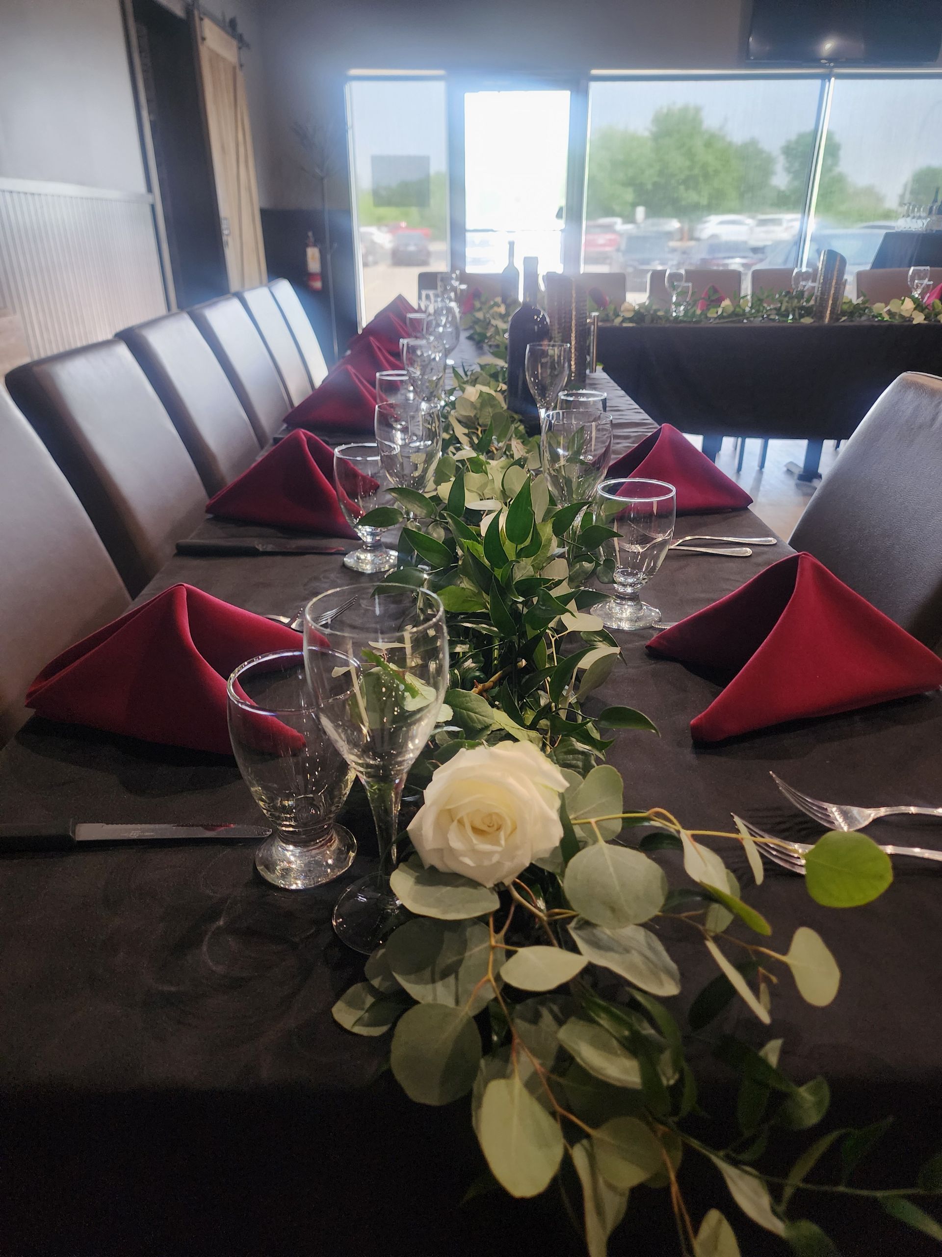 Long dining table set for an event, with red napkins, white floral centerpieces, and black chairs.