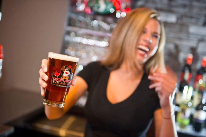 Smiling bartender holding up a pint of amber beer in a lively bar