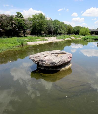 Rock formation in water, with trees and cloudy sky in the background.