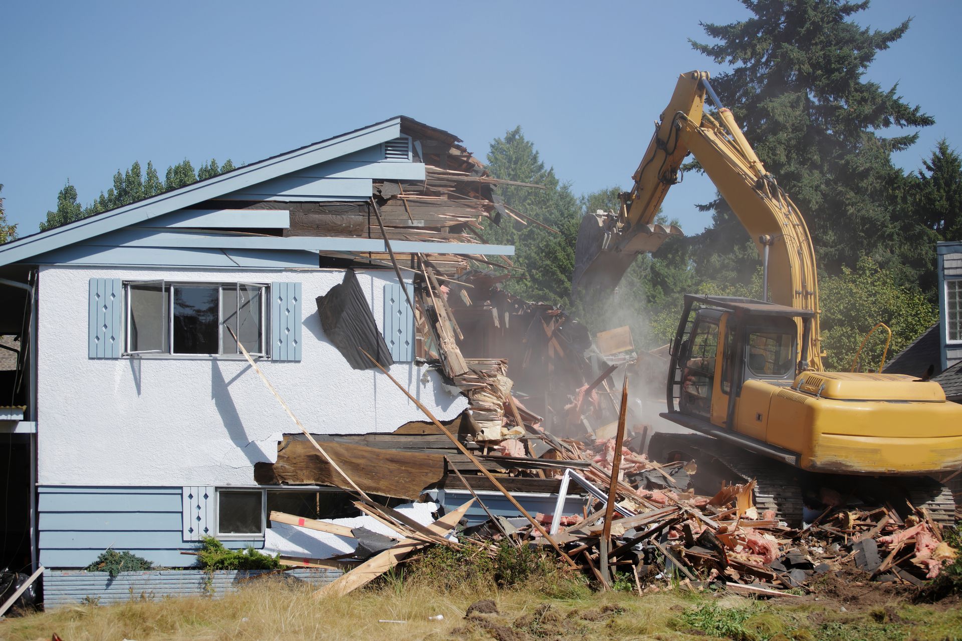 Yellow excavator performing house demolition with debris everywhere.