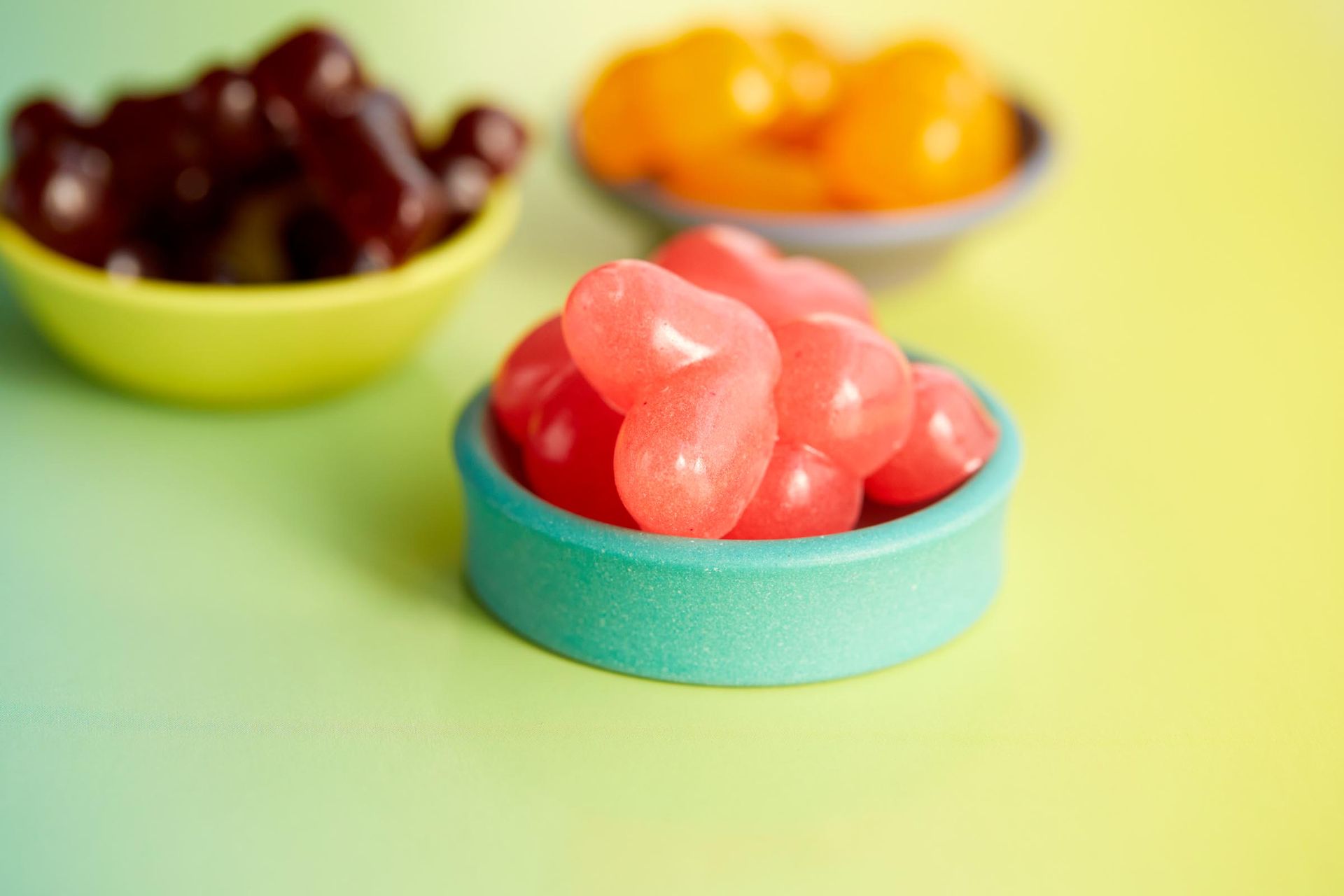 A blue bowl filled with red heart shaped gummies on a table.