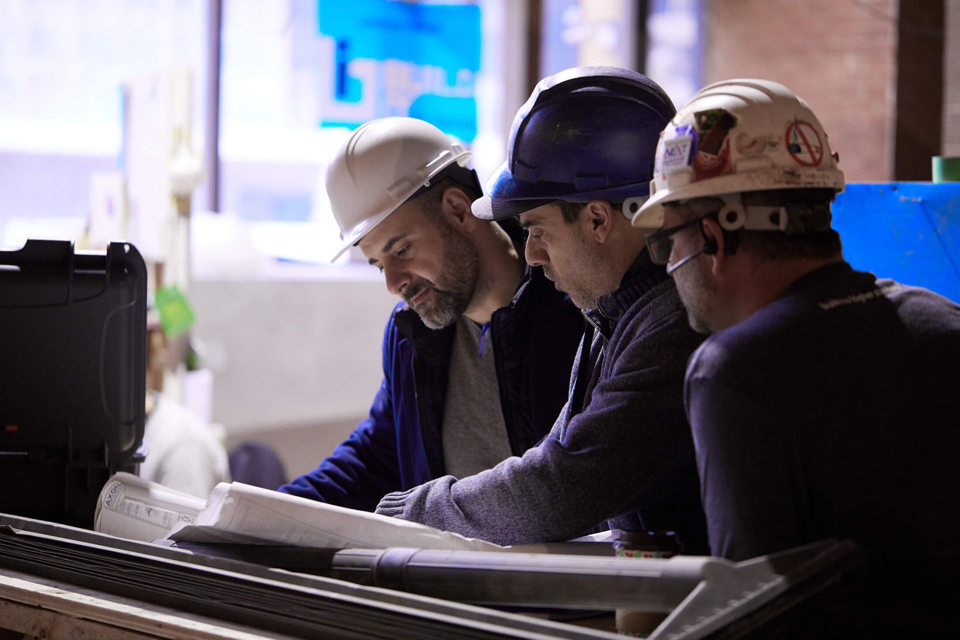 Three men wearing hard hats are looking at a blueprint.