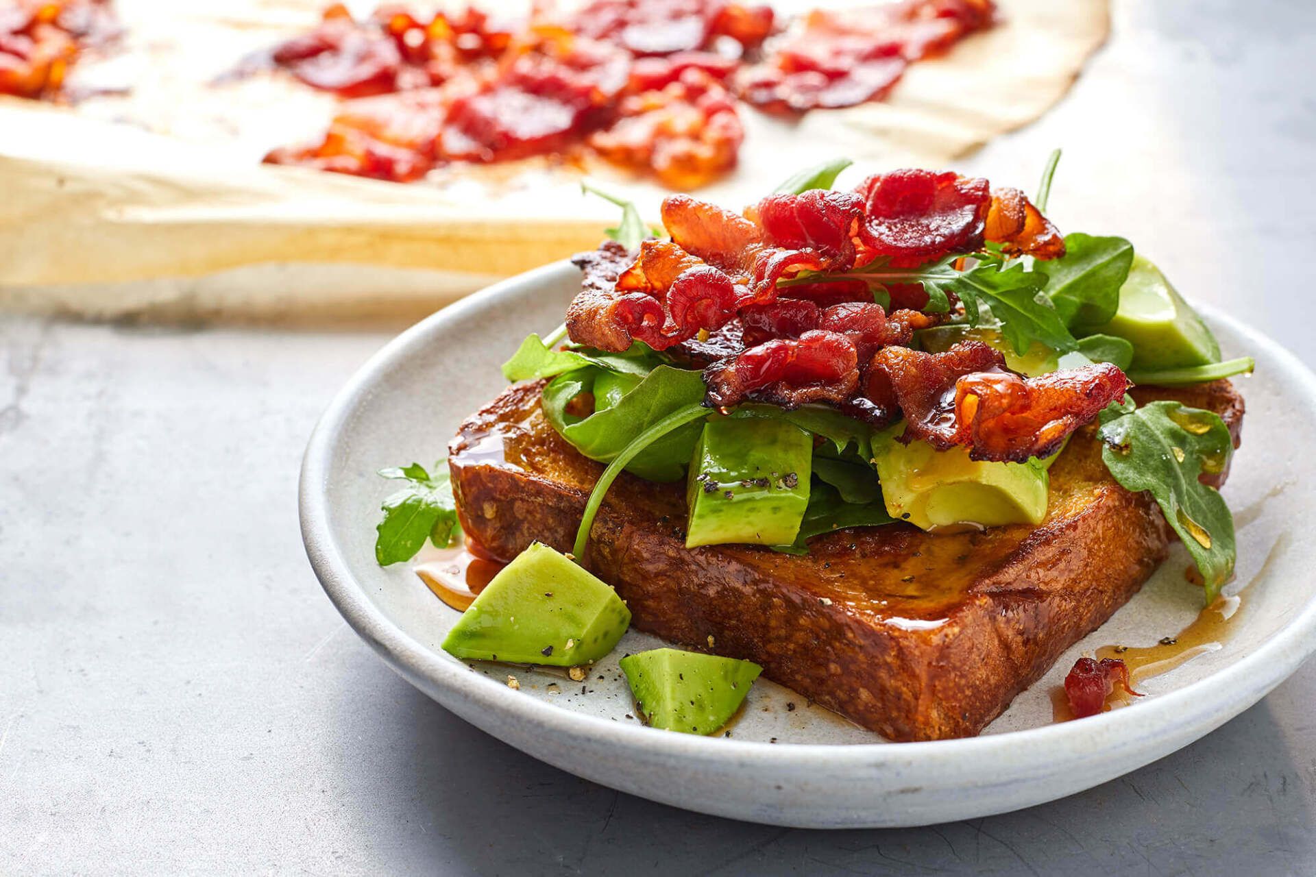 A close up of a plate of food with avocado , bacon and lettuce.