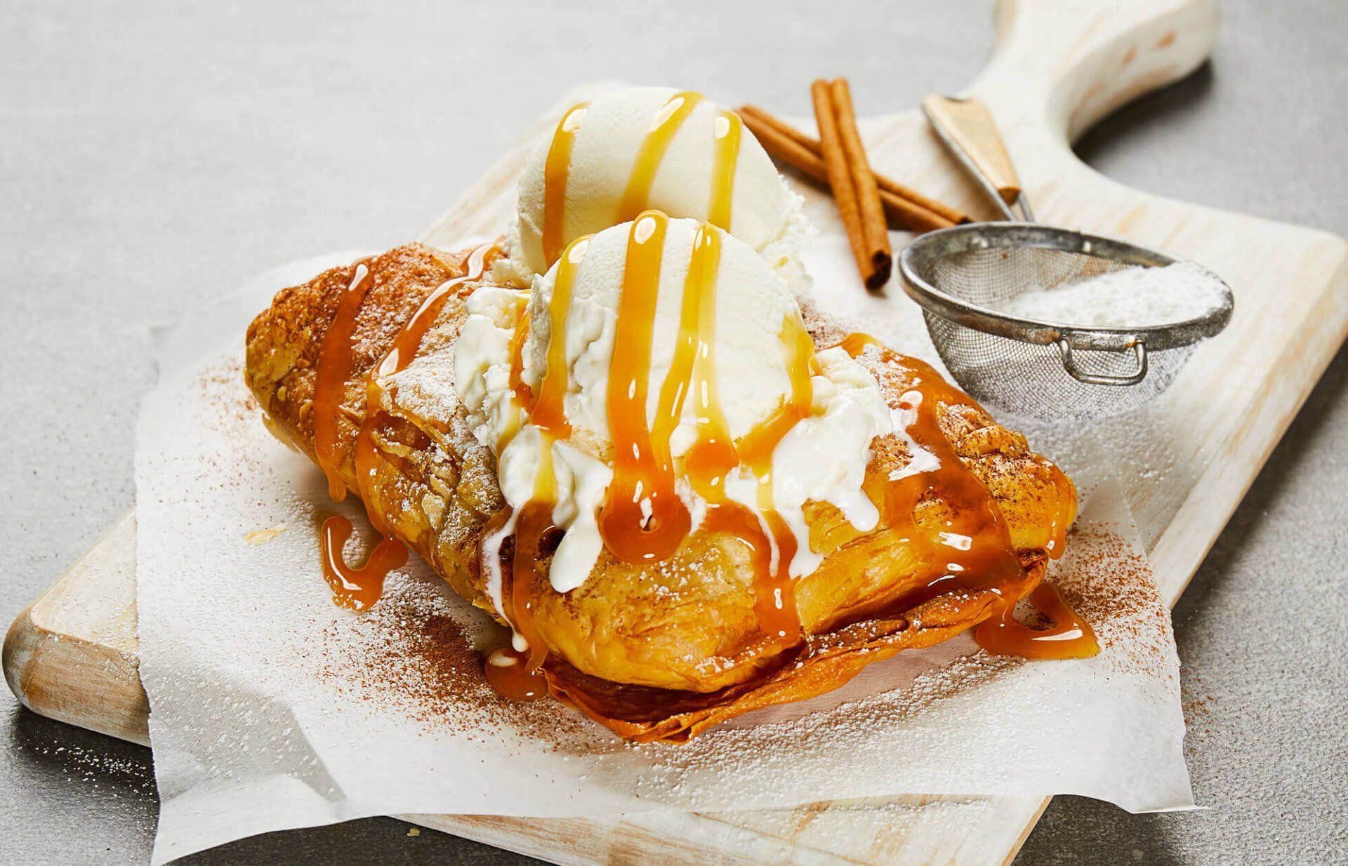 A close up of a dessert with ice cream and caramel sauce on a cutting board.