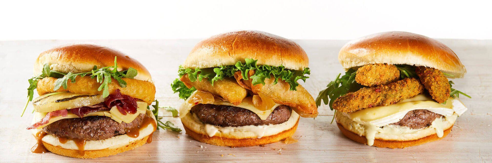 Three hamburgers with different toppings are lined up on a table.