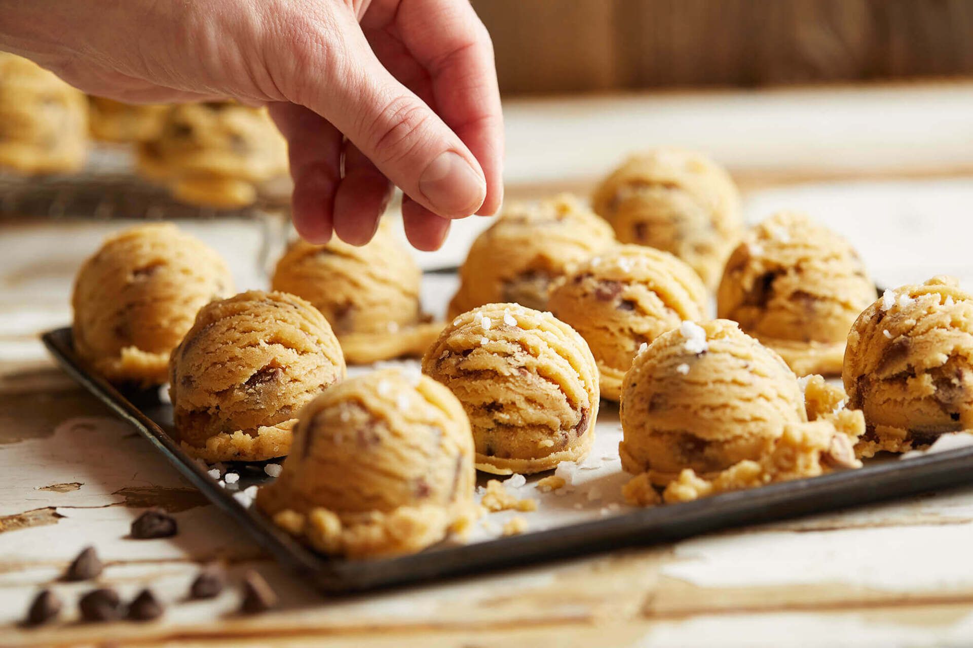 A person is sprinkling sugar on a tray of cookie dough balls.