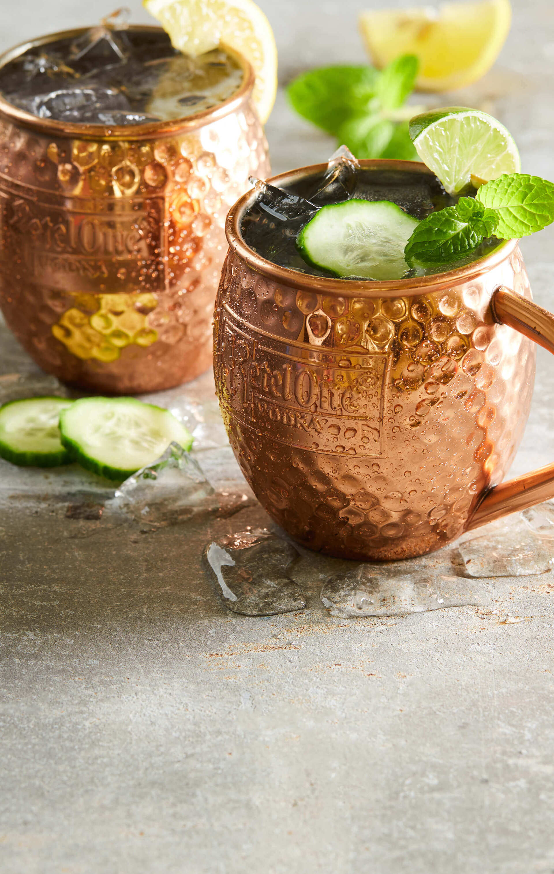 Two copper mugs filled with a drink and cucumber slices on a table.