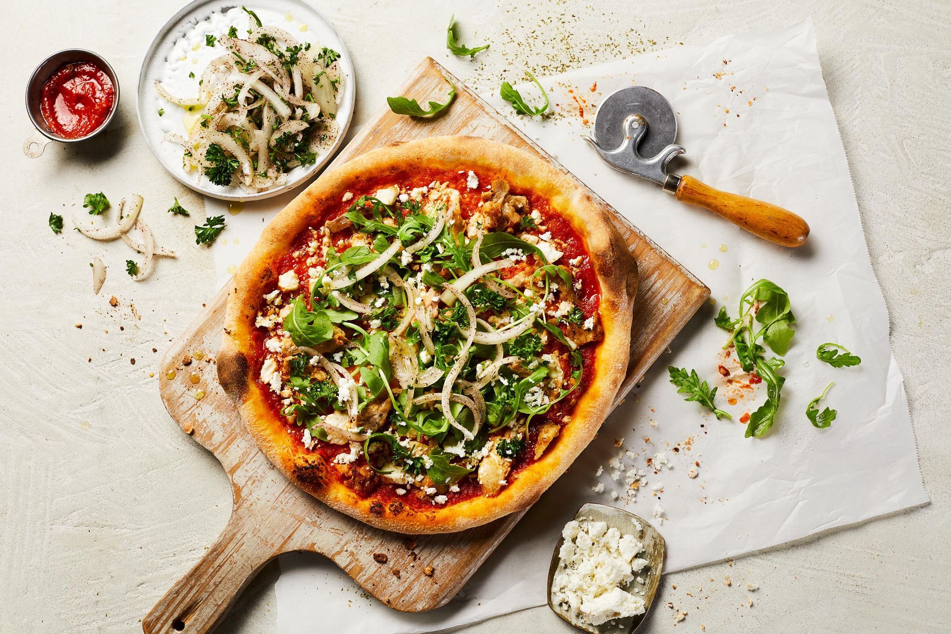 A pizza is sitting on a wooden cutting board next to a pizza cutter.