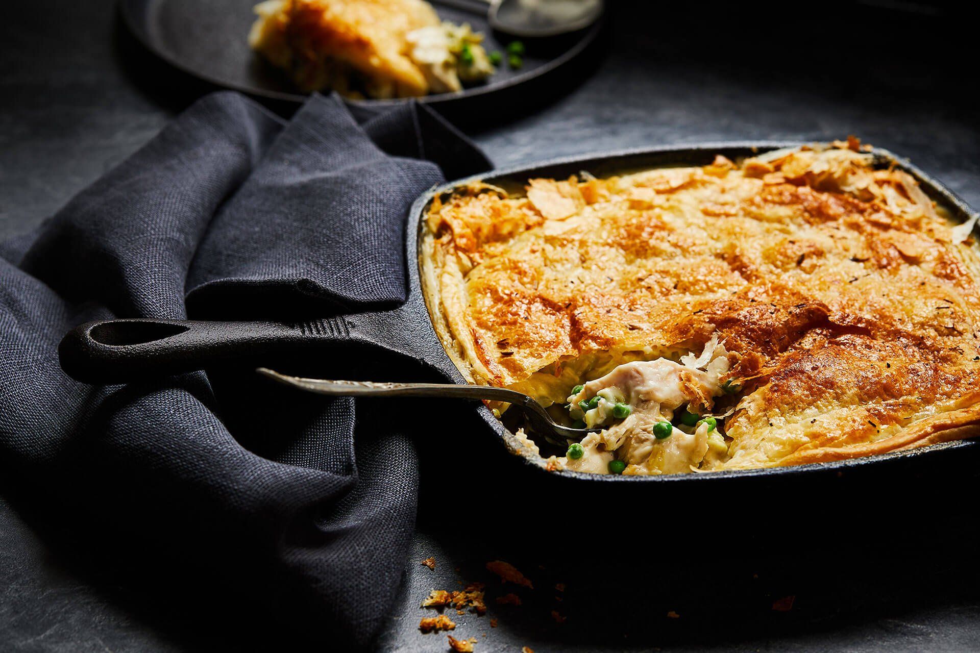 A pot pie with a spoon in it is sitting on a table.