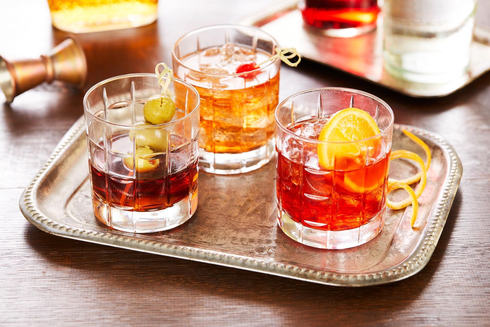 Three different types of drinks are on a silver tray on a wooden table.