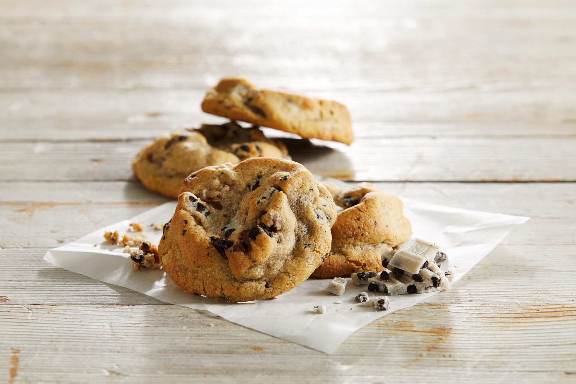 A stack of chocolate chip cookies on a piece of wax paper on a wooden table.