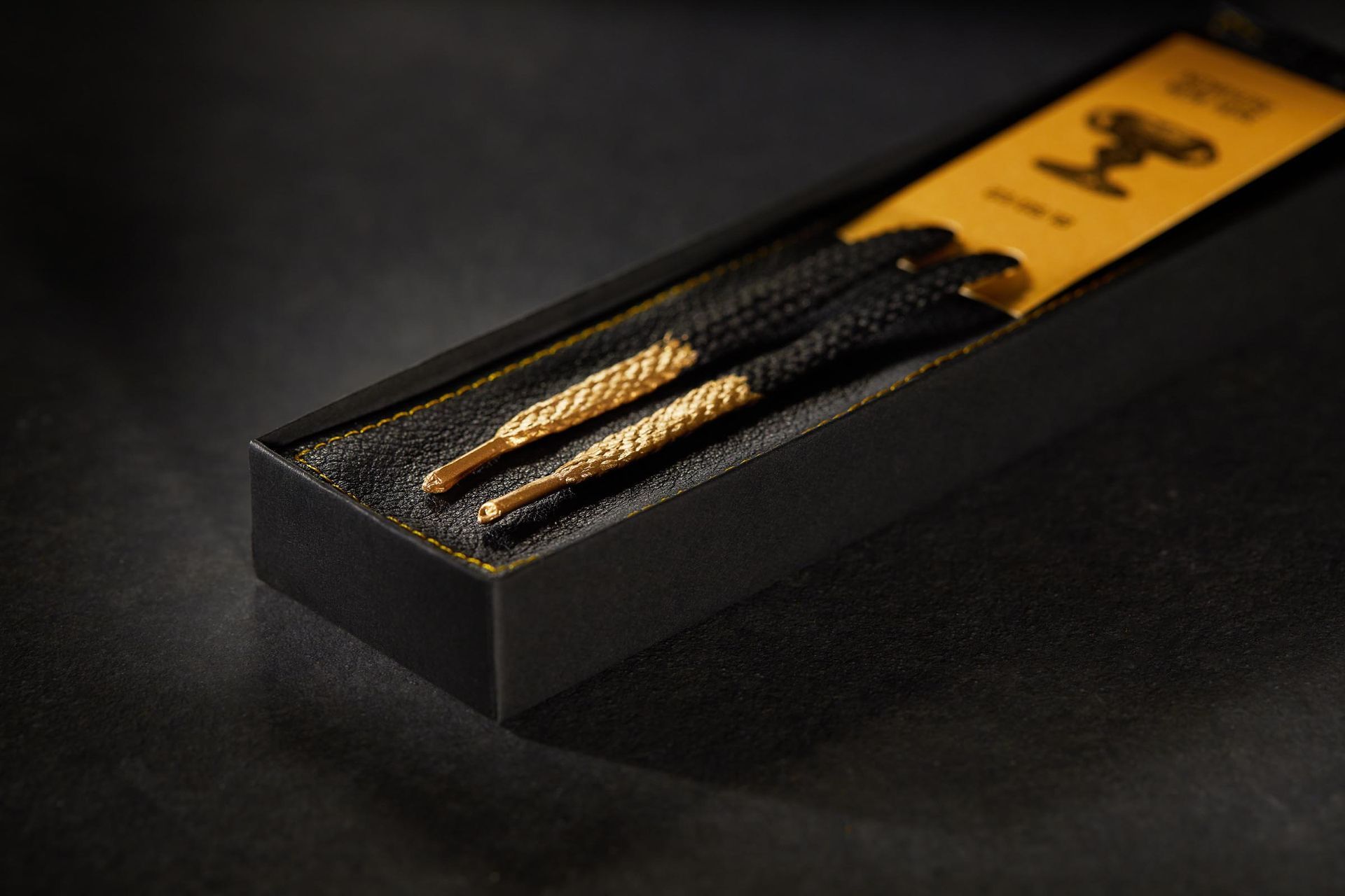 A pair of black and gold shoe laces in a black box
