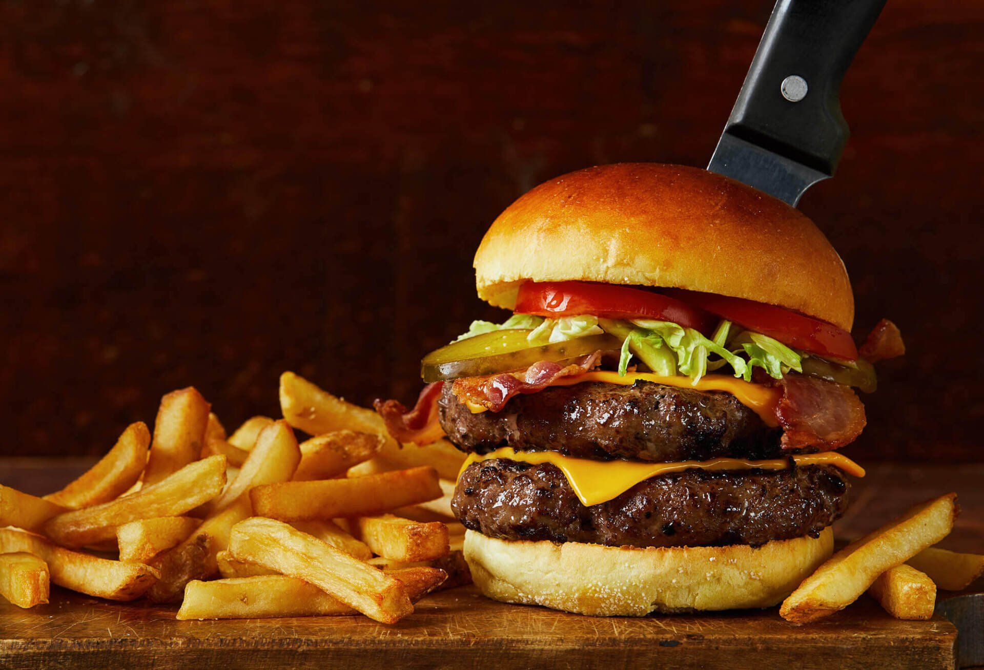A double cheeseburger and french fries on a wooden cutting board.