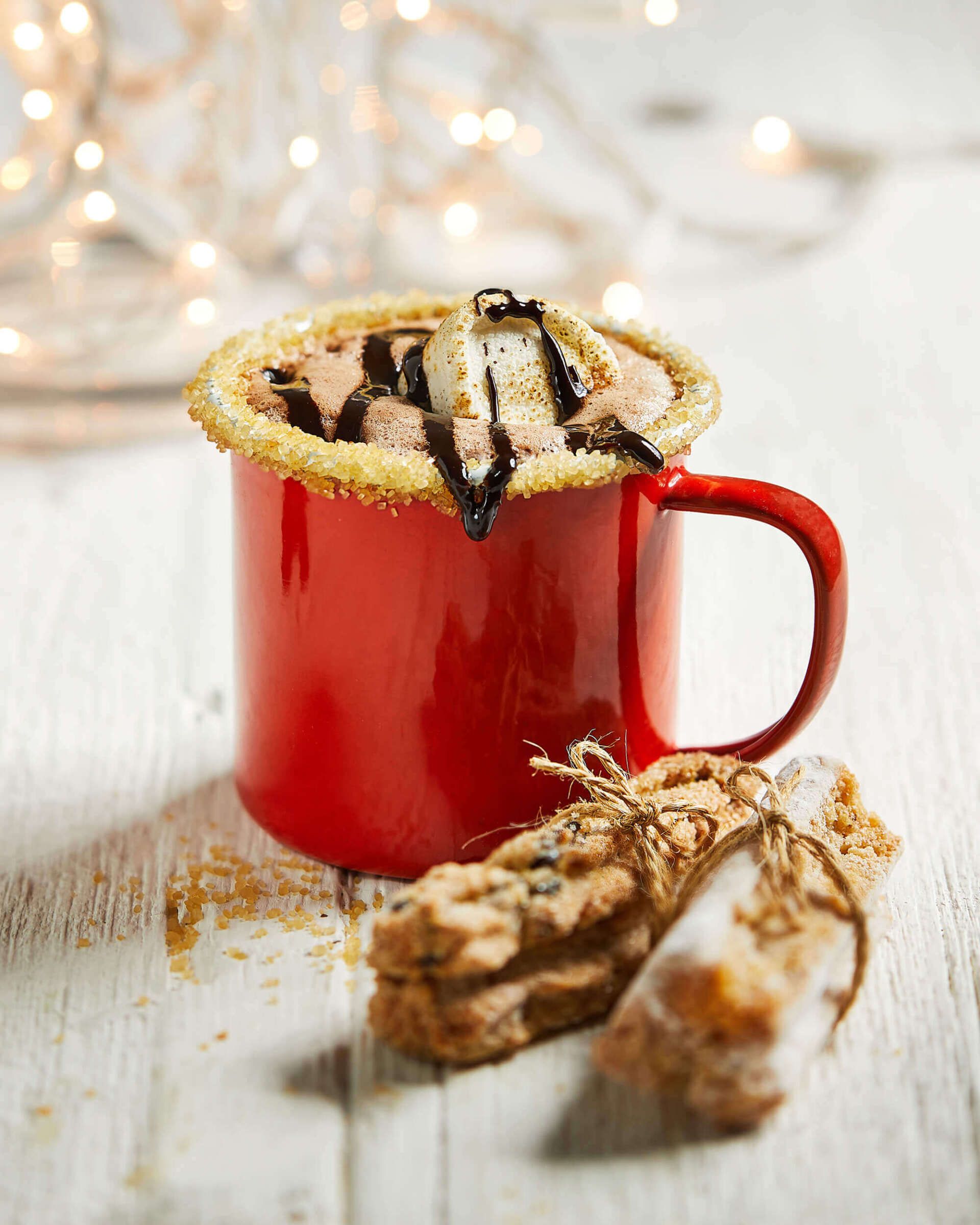 A red mug of hot chocolate with marshmallows and chocolate sauce