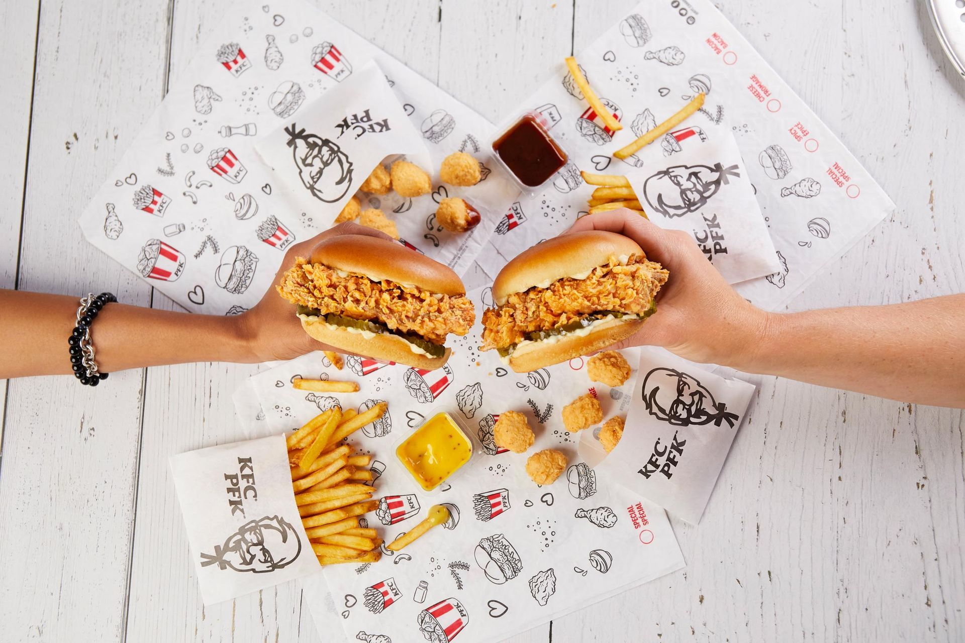 Two people are holding chicken sandwiches and french fries on a table.