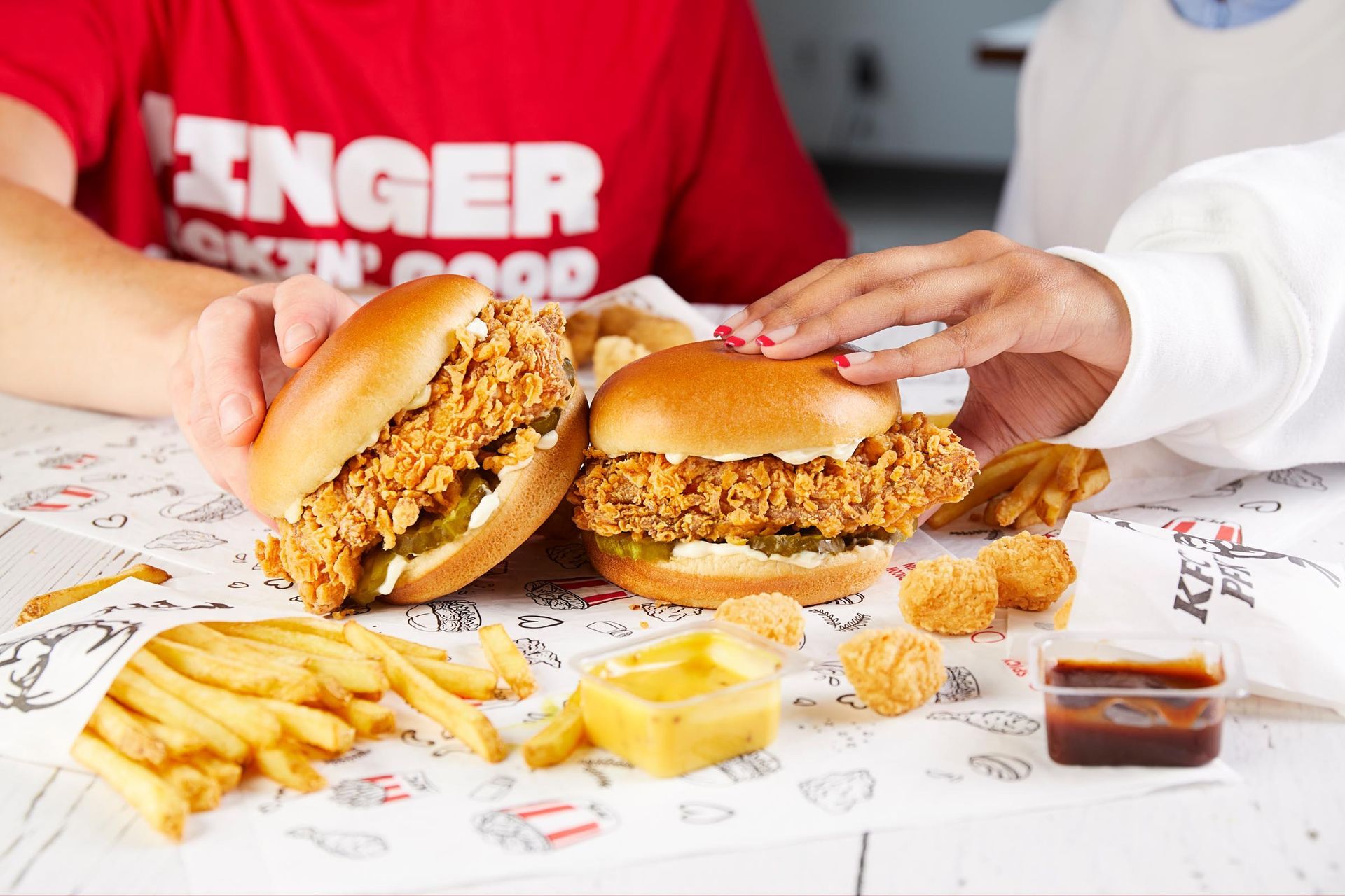Two people are sitting at a table eating chicken sandwiches and french fries.