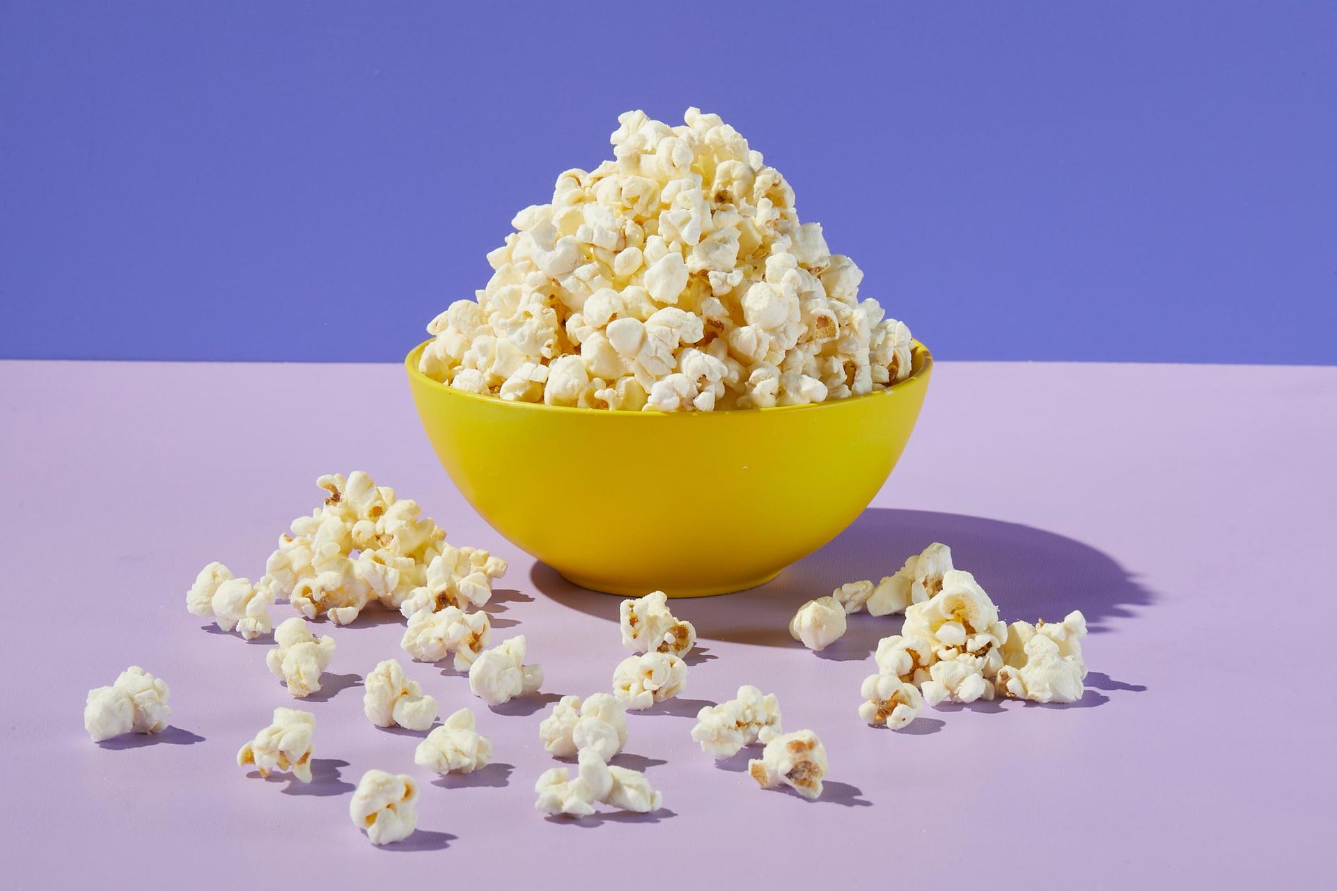 A yellow bowl filled with popcorn on a purple table.