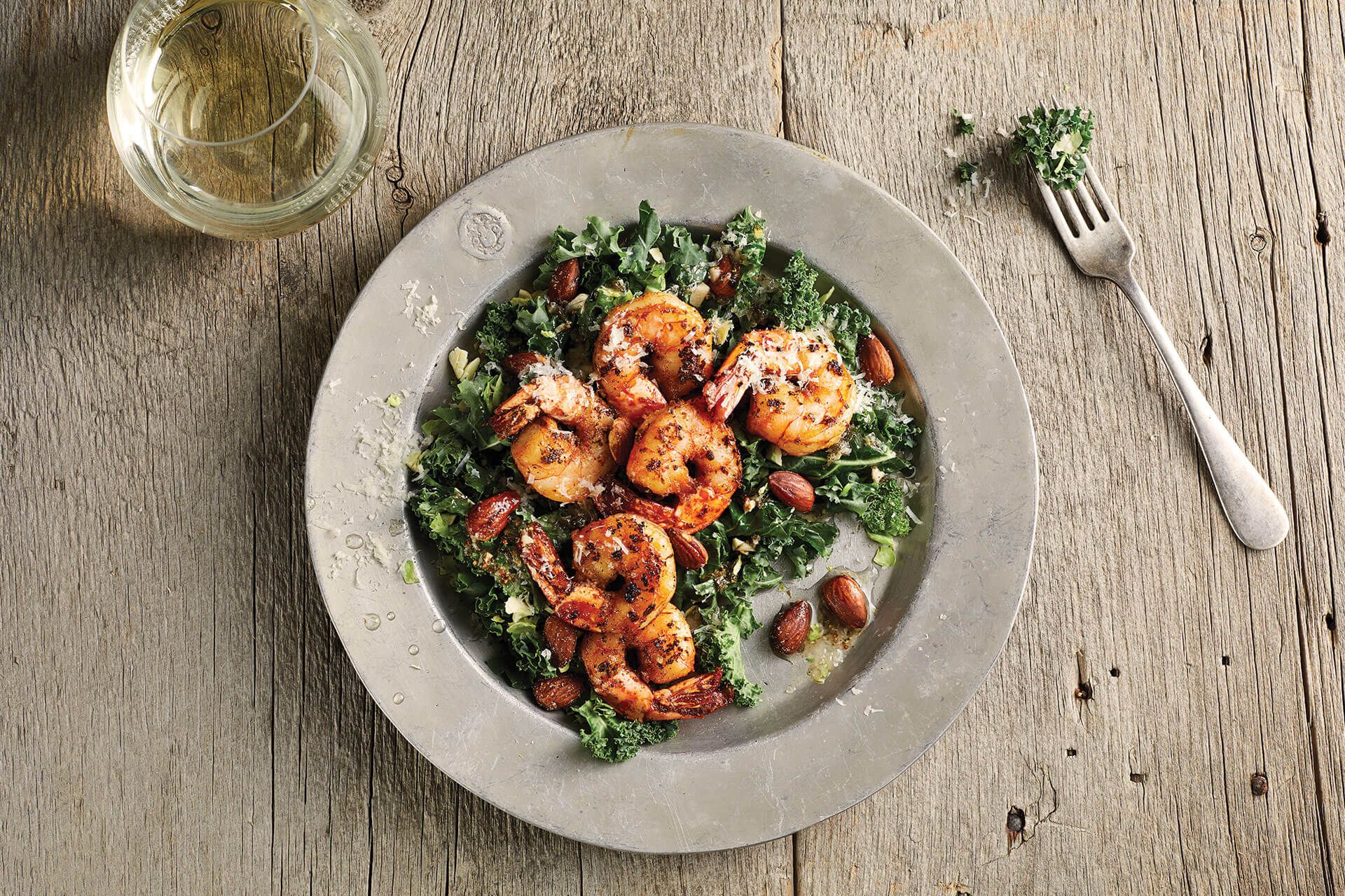 A plate of shrimp and kale salad with a fork on a wooden table.
