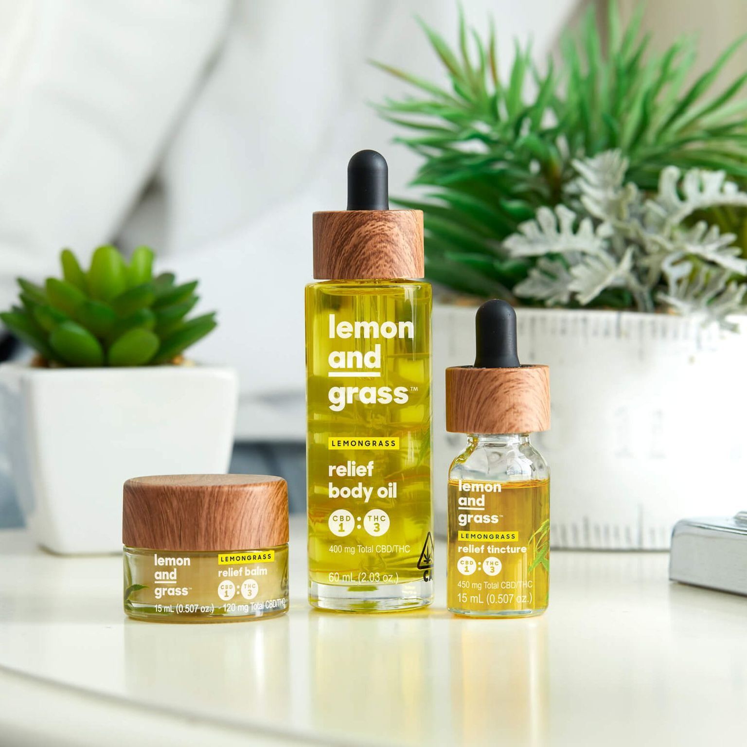 Three bottles of lemon and grass relief body oil are sitting on a table.