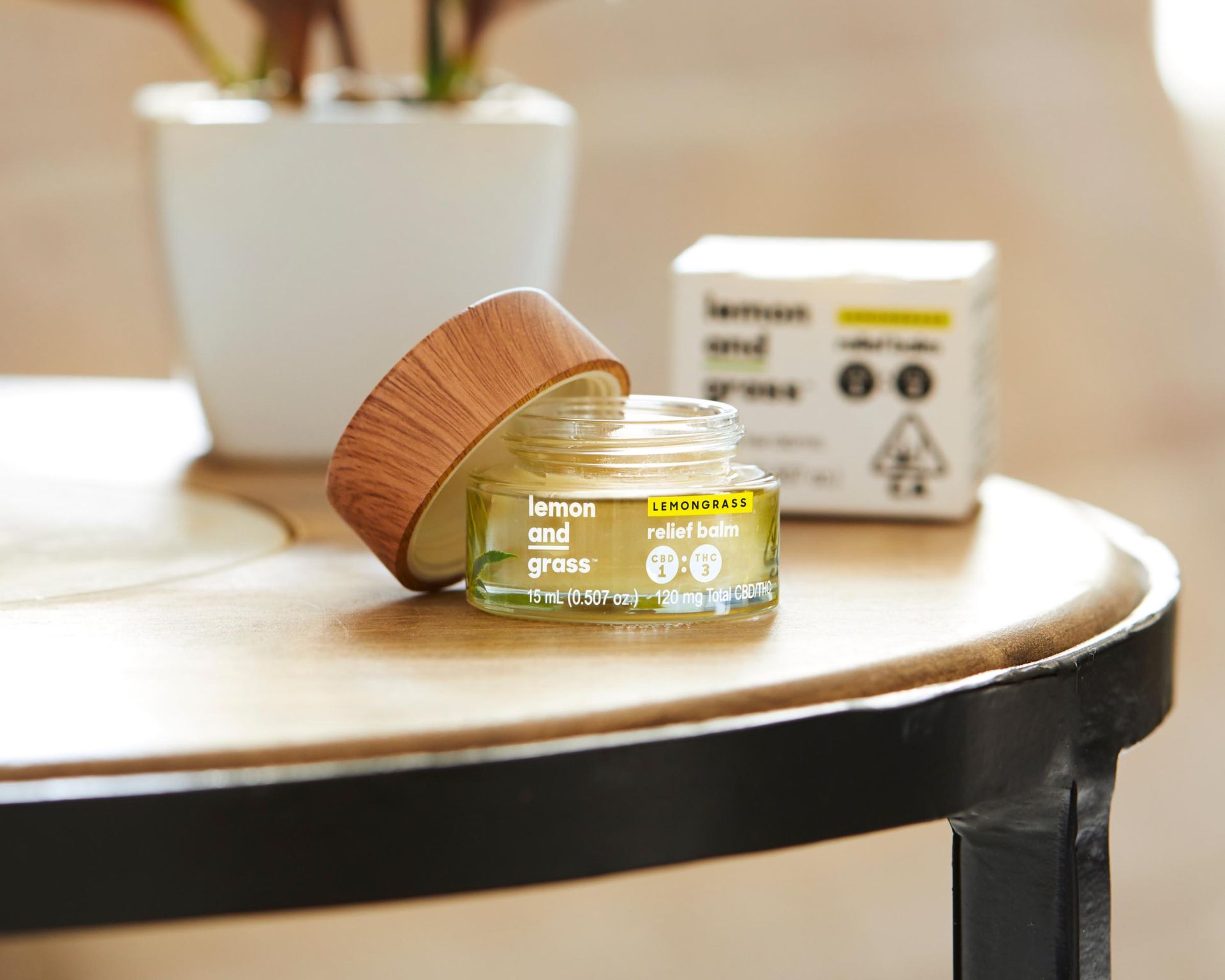 A small jar of cream is sitting on a wooden table next to a plant.