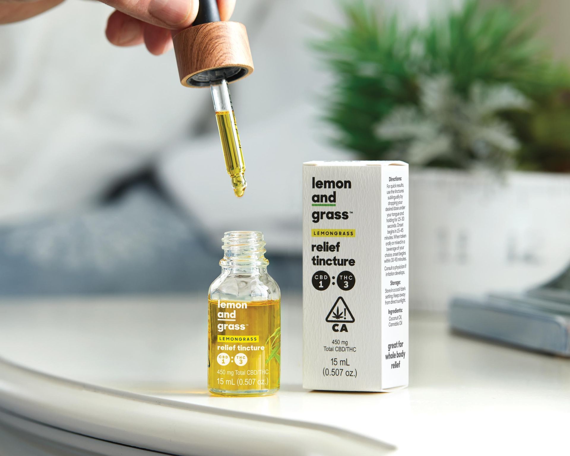 A person is holding a bottle of lemon and grass relief tincture next to a box.