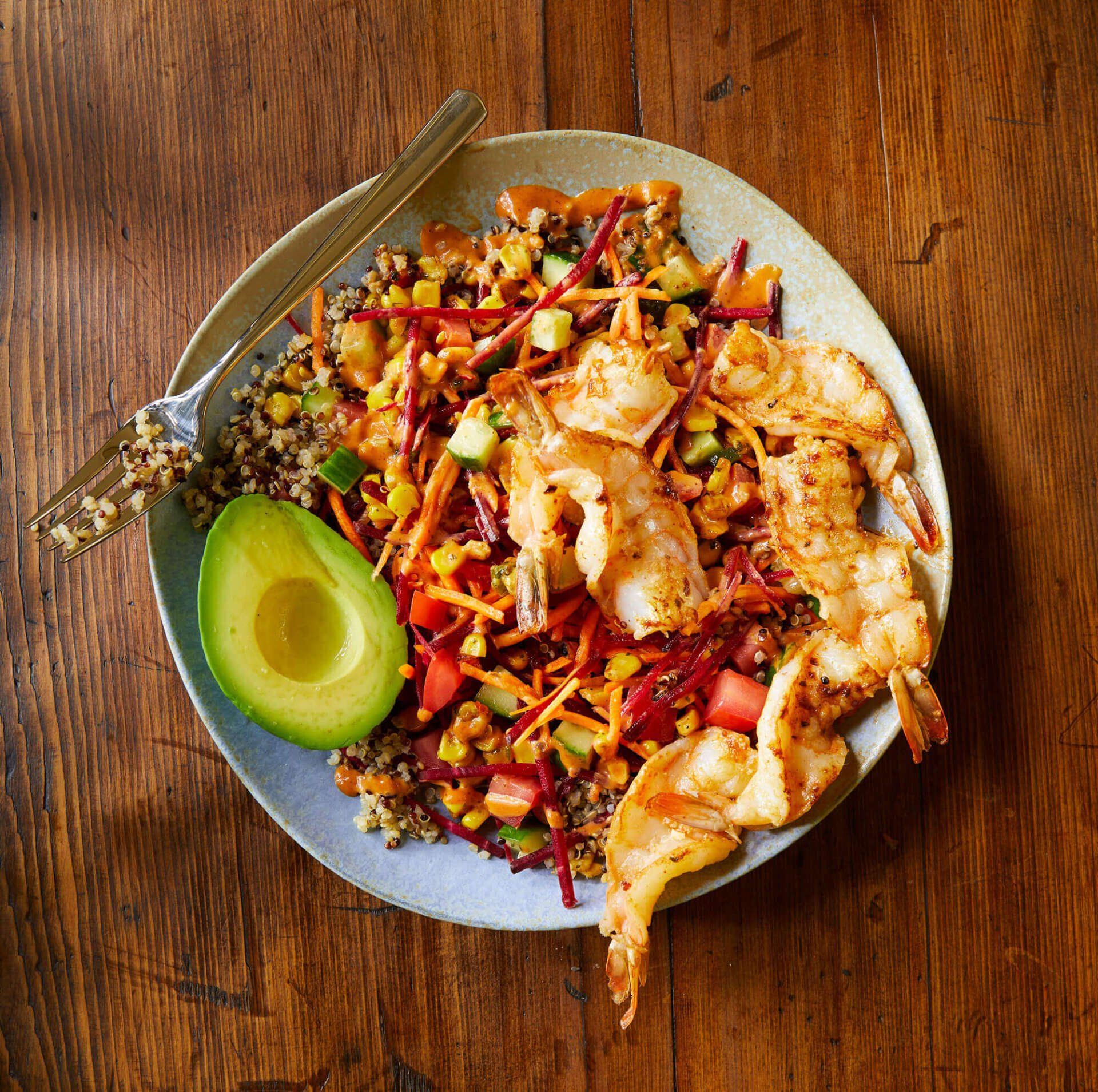 A plate of food with avocado and shrimp on a wooden table