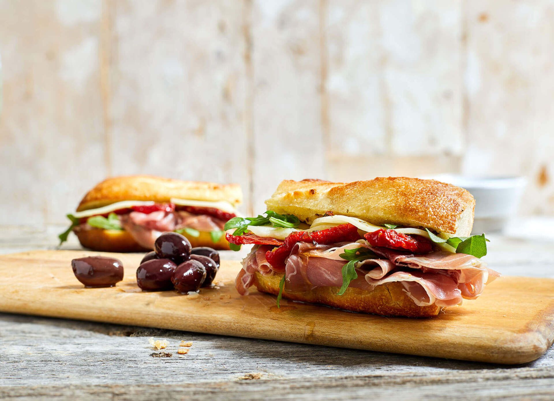 Two sandwiches are sitting on a wooden cutting board.