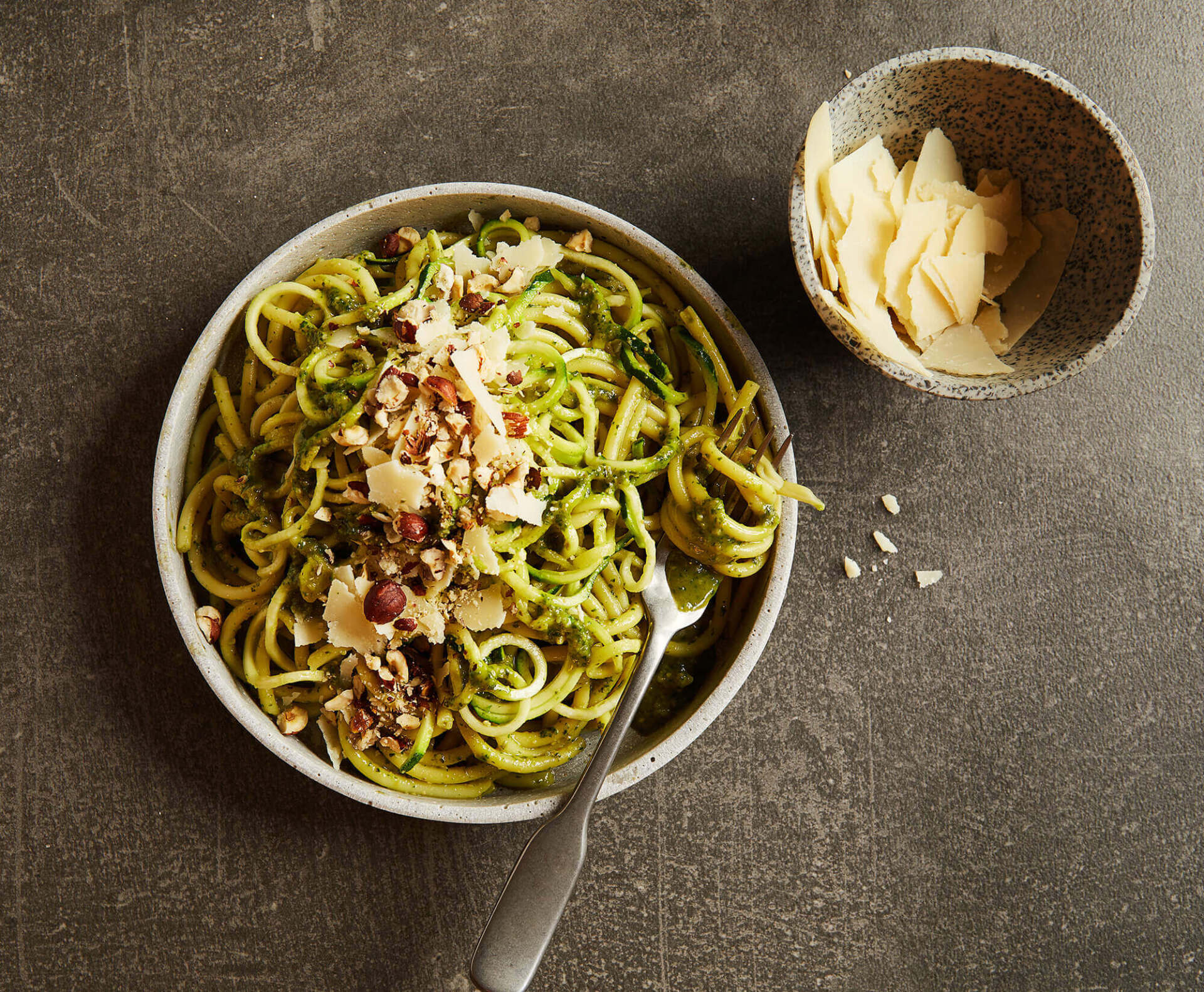 A bowl of noodles with nuts and cheese next to a bowl of cheese