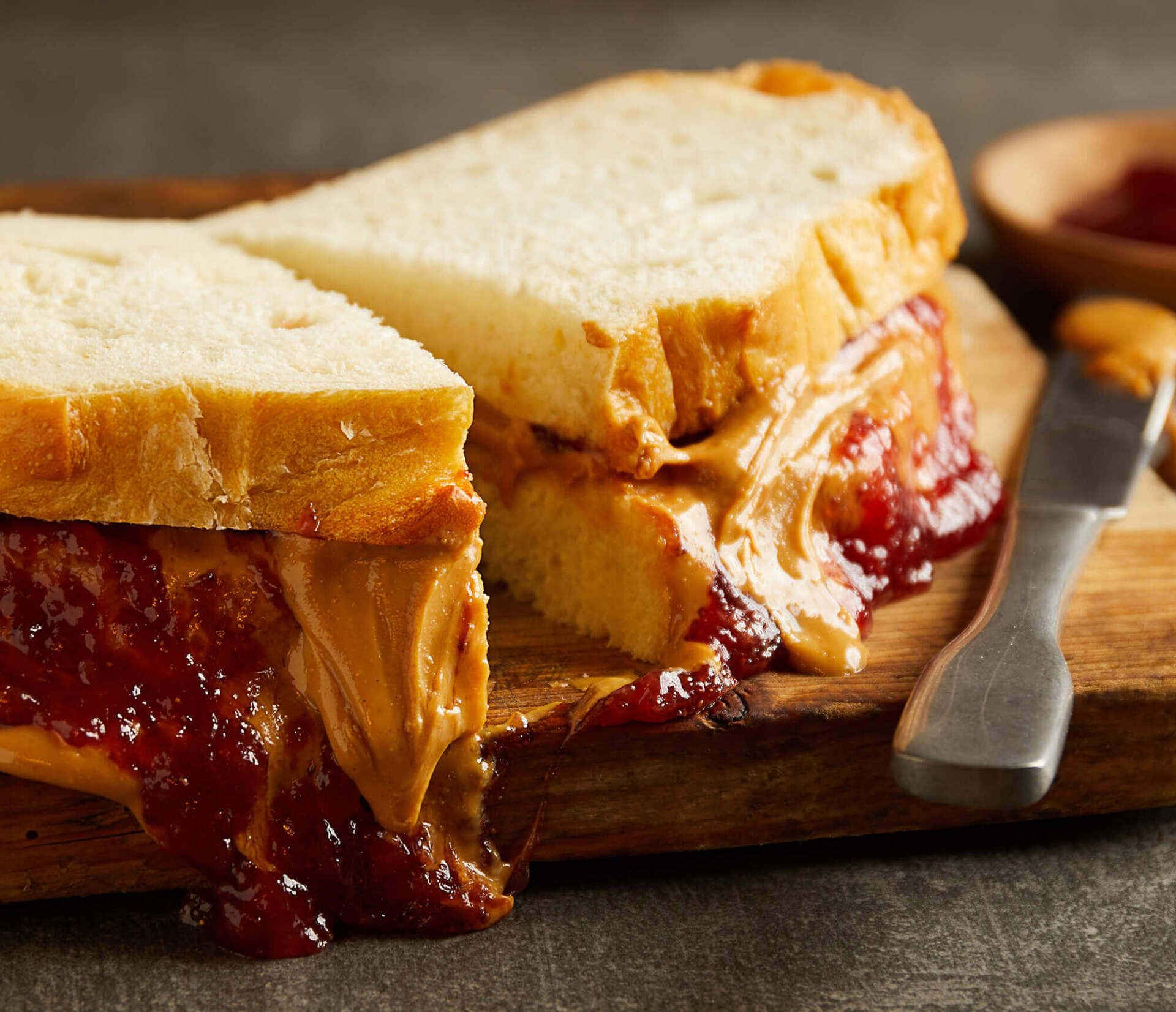 A peanut butter and jelly sandwich is cut in half on a cutting board