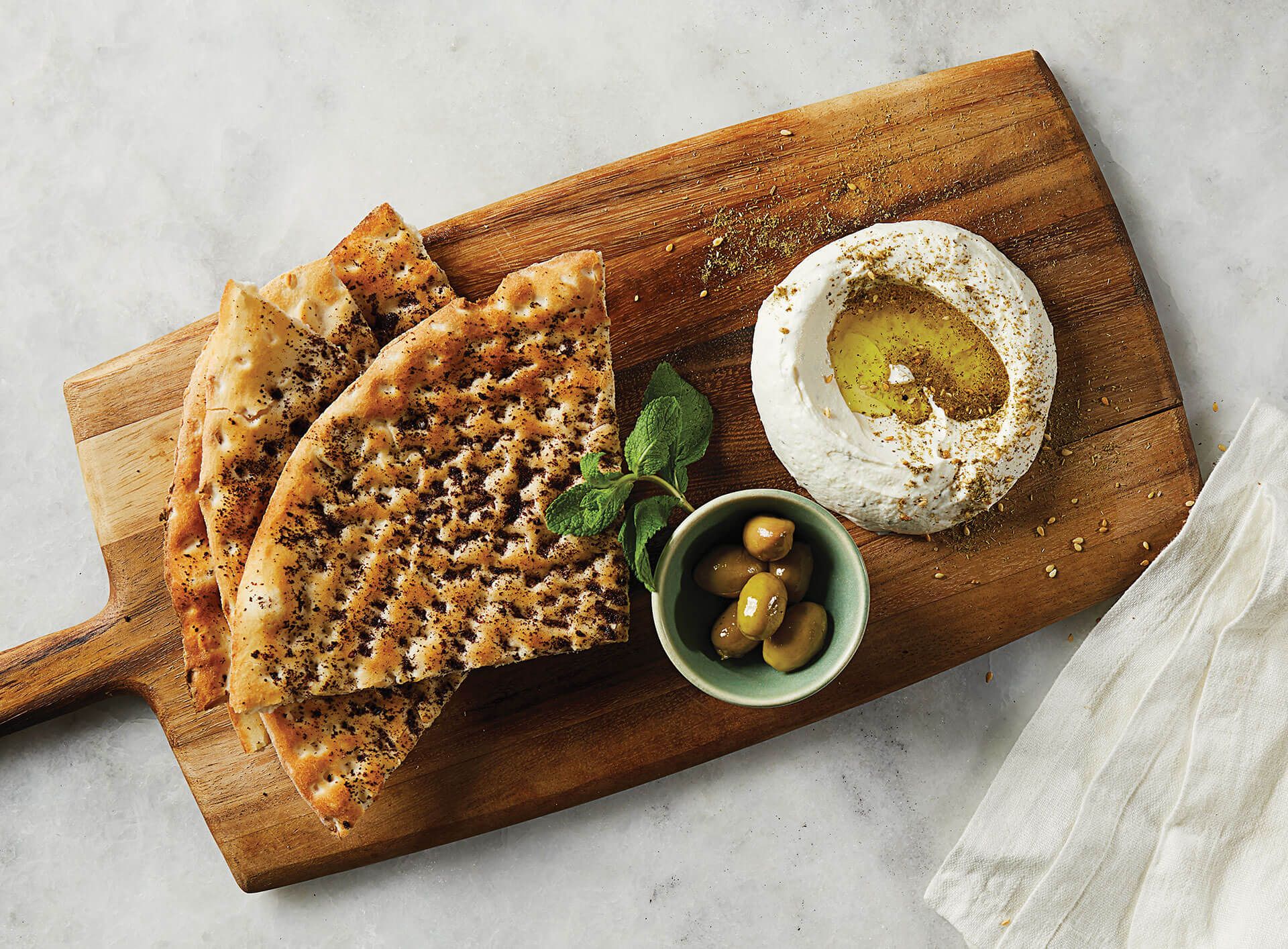 A wooden cutting board topped with bread , hummus and olives.