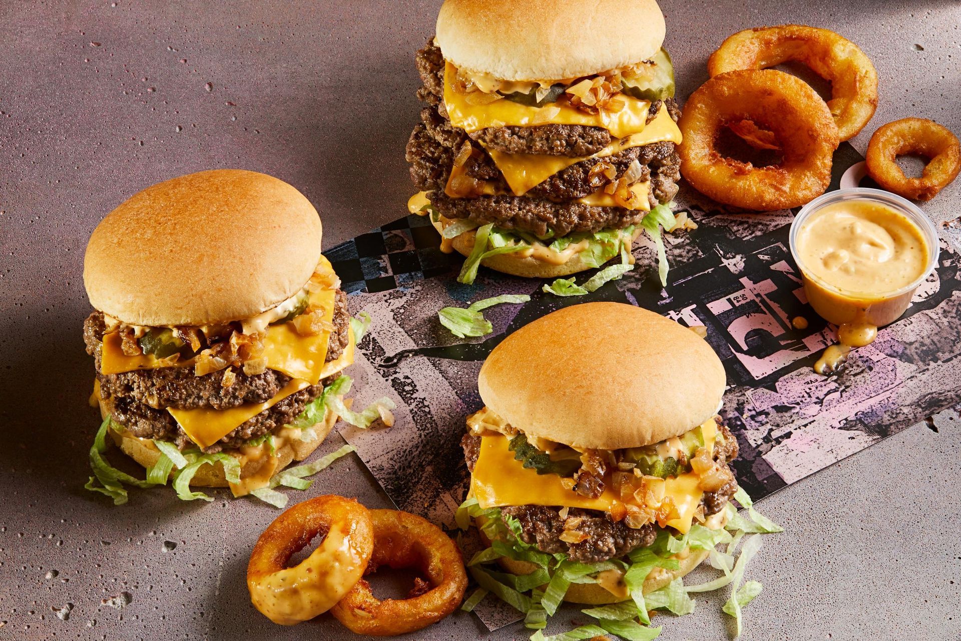 Three hamburgers and onion rings are sitting on a table.