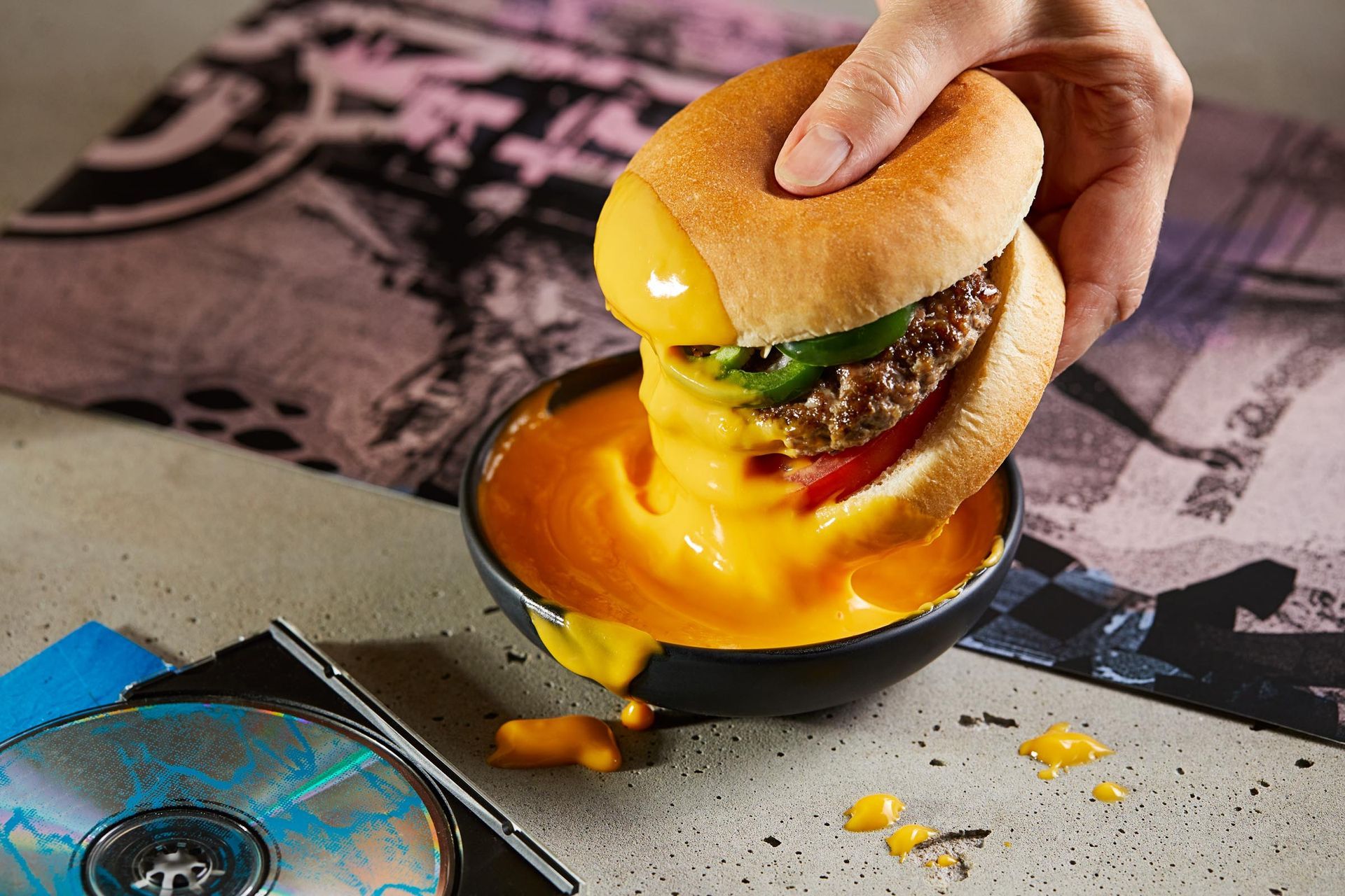 A person is dipping a hamburger in a bowl of cheese sauce.