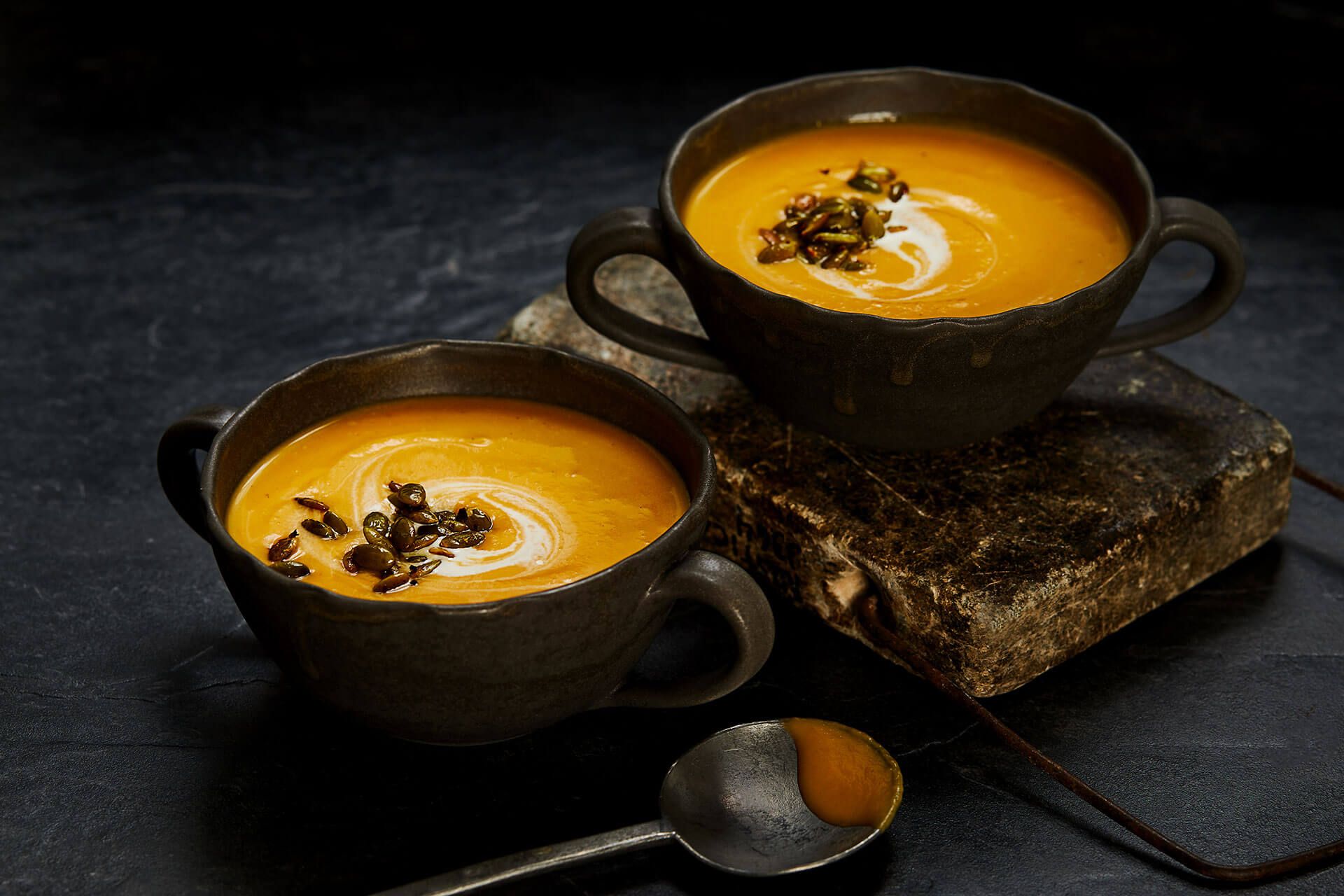 Two cups of soup with spoons on a table.