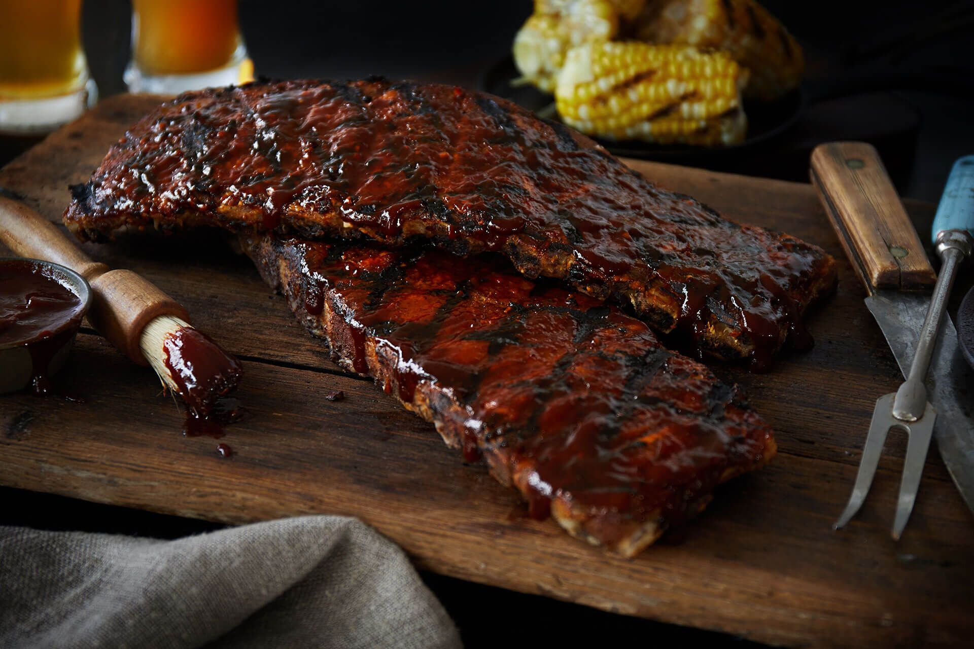 The ribs are sitting on a wooden cutting board with a brush and fork.