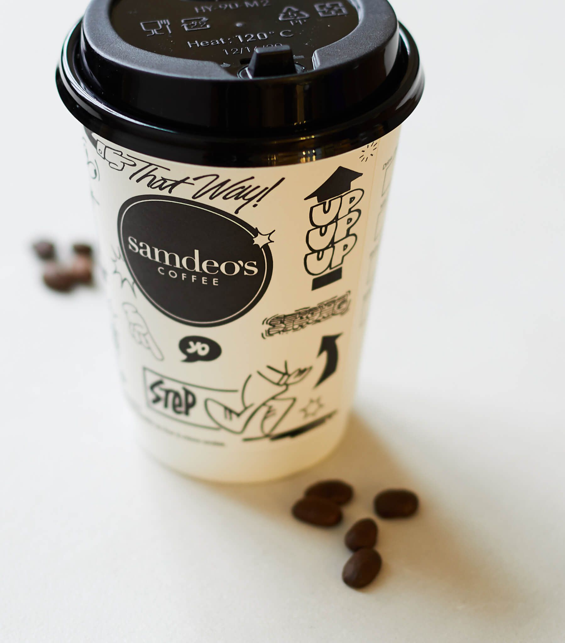 A cup of samdeos coffee sits next to some coffee beans