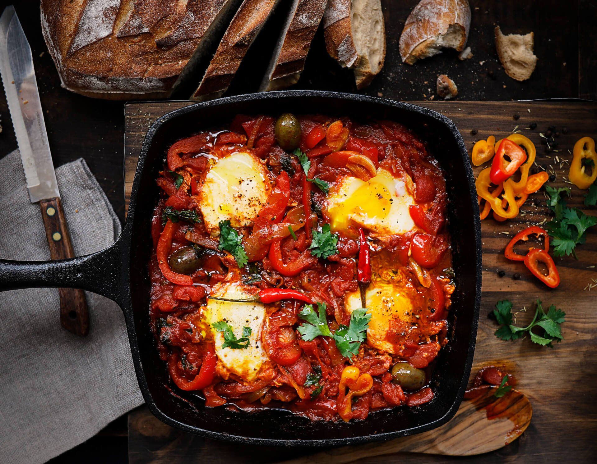A skillet filled with eggs , peppers , olives and tomato sauce.