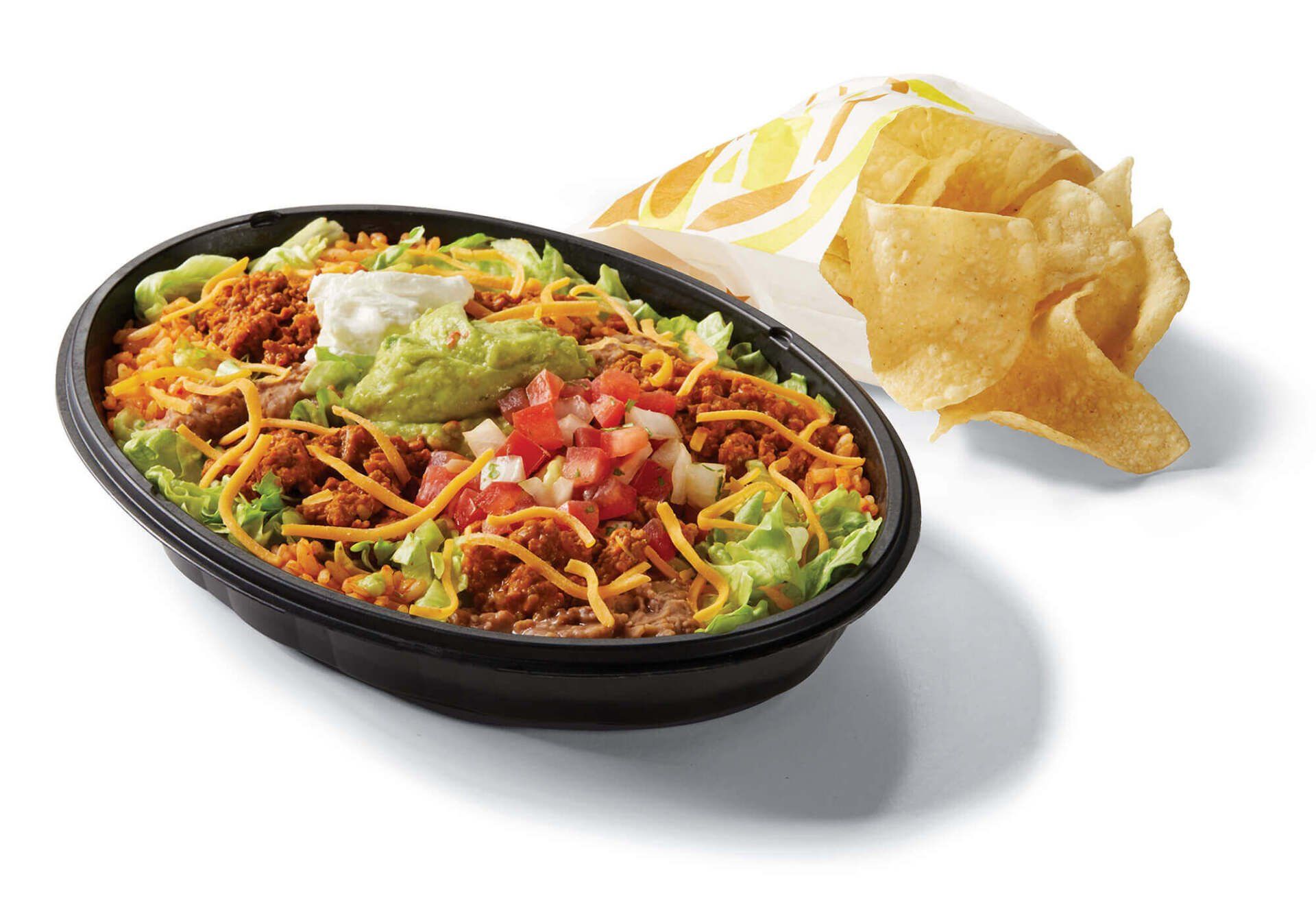 A bowl of taco bell food next to a bag of tortilla chips.