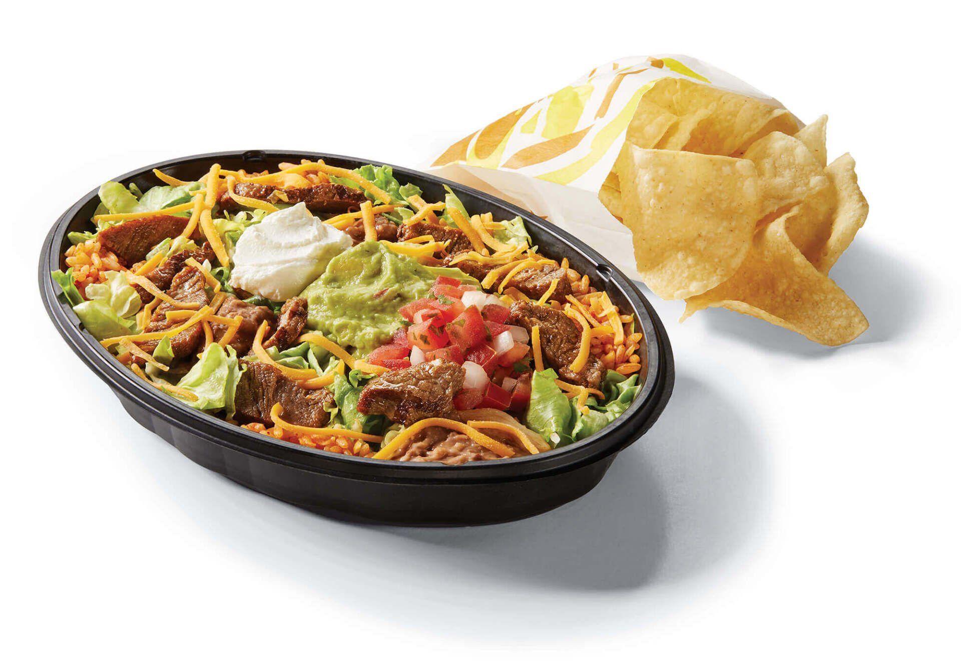 A bowl of taco bell food next to a bag of tortilla chips.
