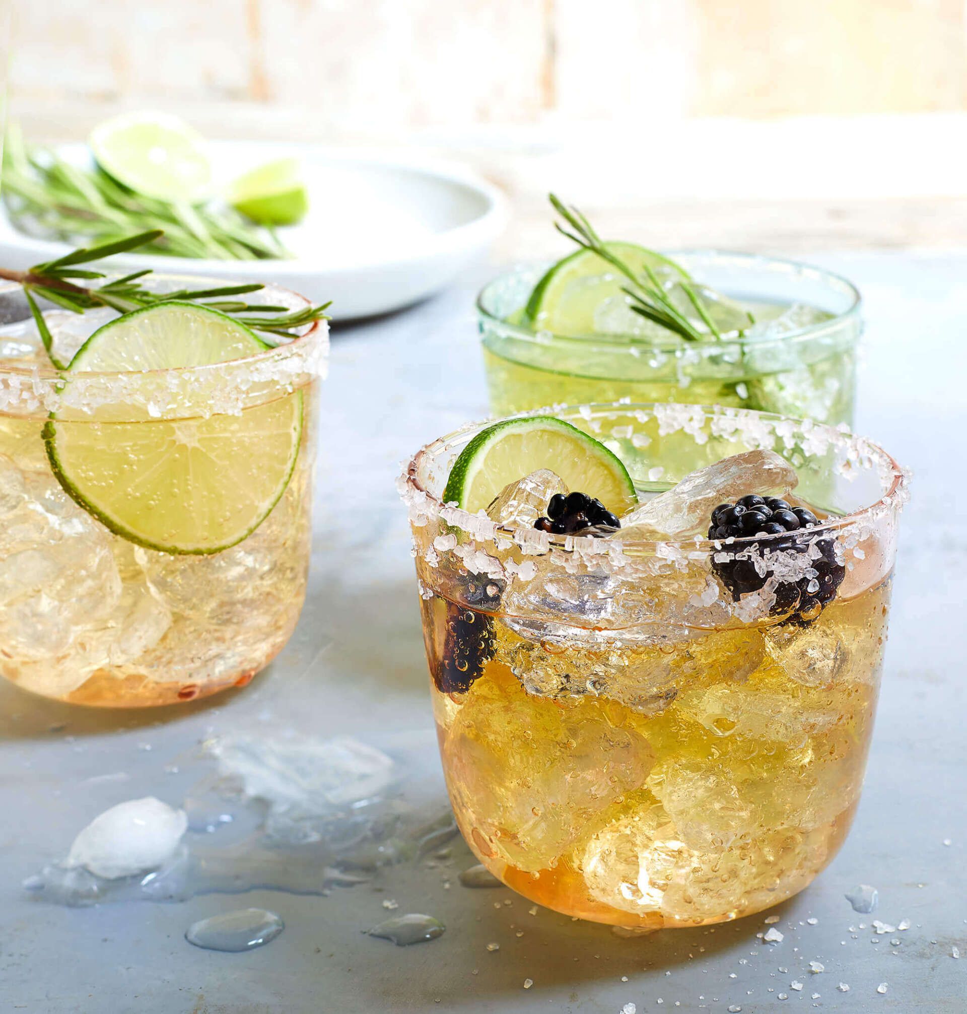 Three glasses of drinks with ice and limes on a table